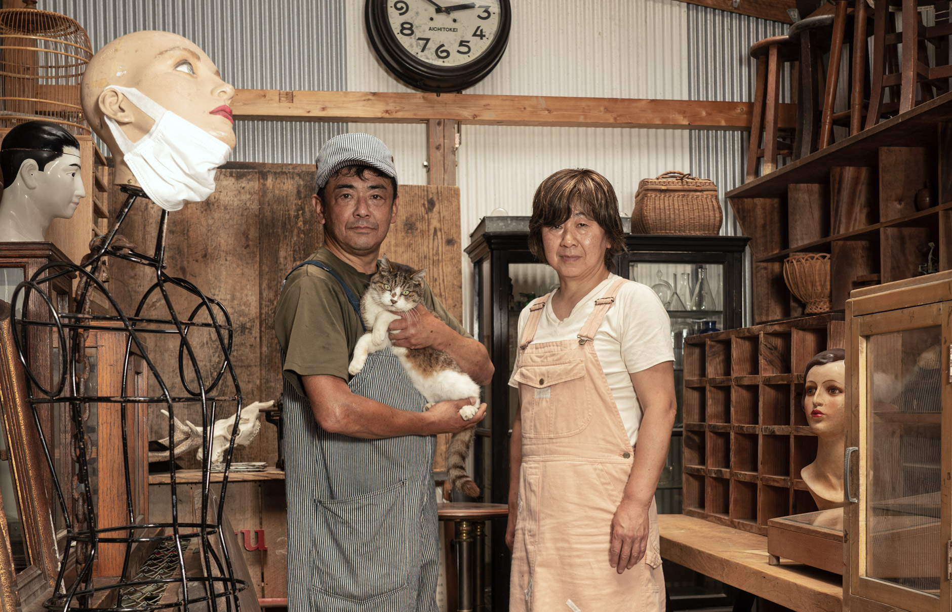 【写真】古道具が並ぶ倉庫の中で、妻と猫とともに佇む 西川さとしさん