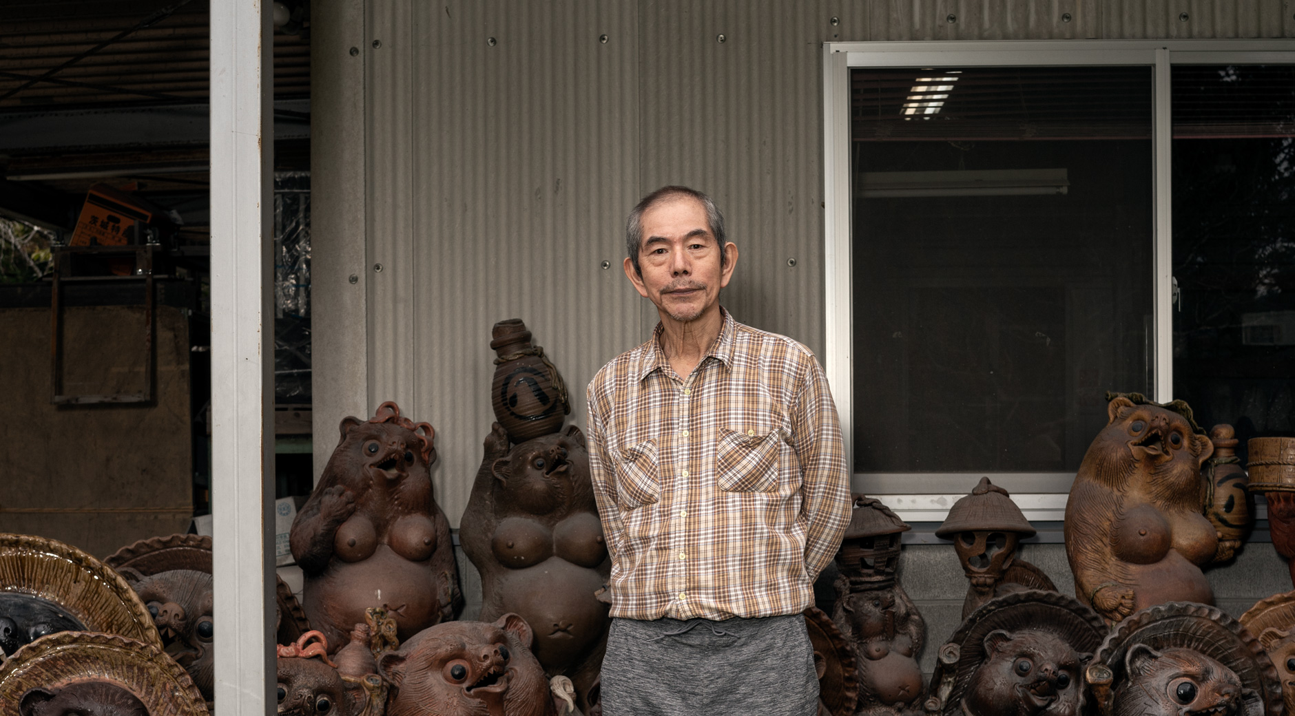 【画像】たくさんの狸の焼き物の中に立つ藤原康造さん