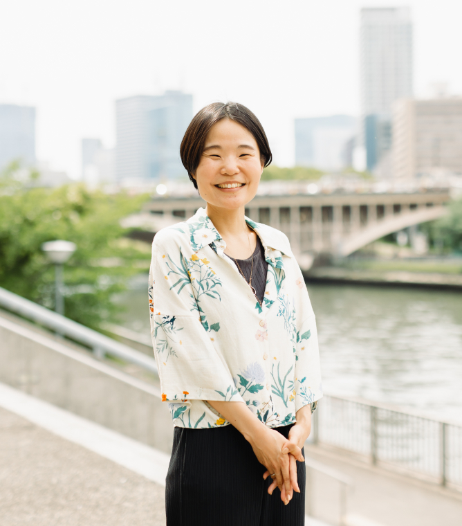 【写真】川縁に佇み、こちらを向く女性