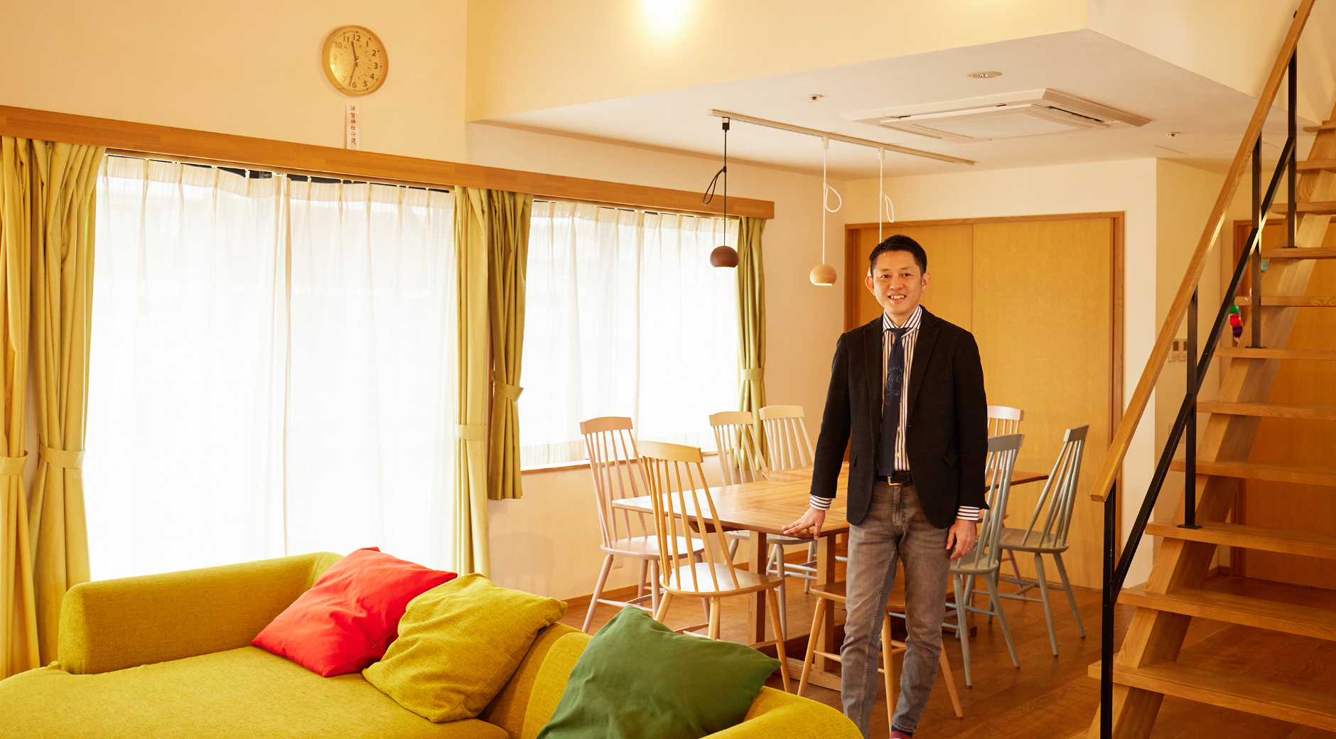 【写真】広いリビングで、ソファーの奥、ダイニングテーブルの前に立ち笑顔を向ける男性