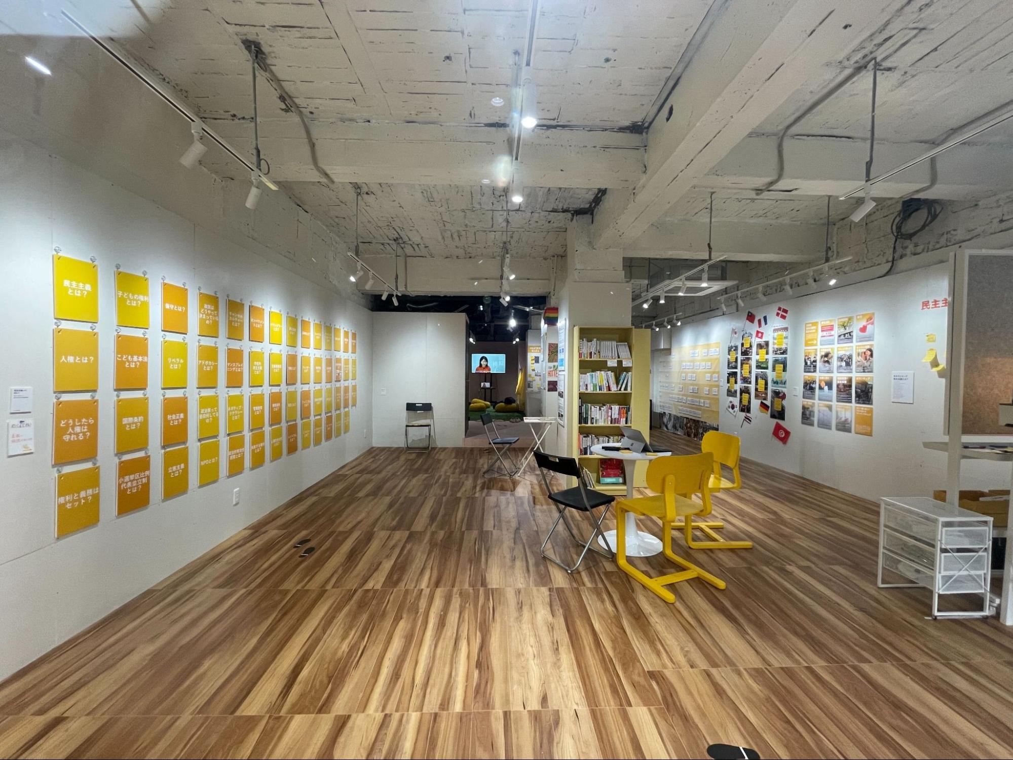【写真】博物館の内観。左側にパネル、右側に写真展示が多数あり、中央の柱近辺に書籍などが、奥の部屋にはモニターが見える