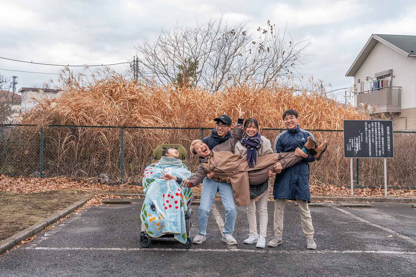 冬の無人の駐車場で、山本さんの4人の子どもたちに抱えられて笑う山本さんのポートレート。