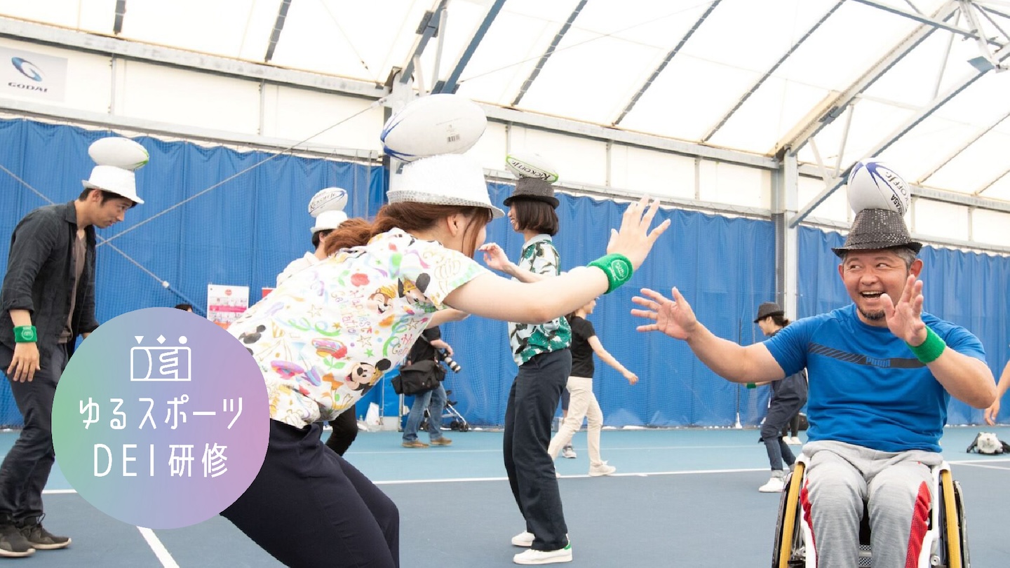 【写真】ハットラグビーをしている様子。車椅子の男性と女性が頭にラグビーボールが乗った帽子をかぶって向き合っている