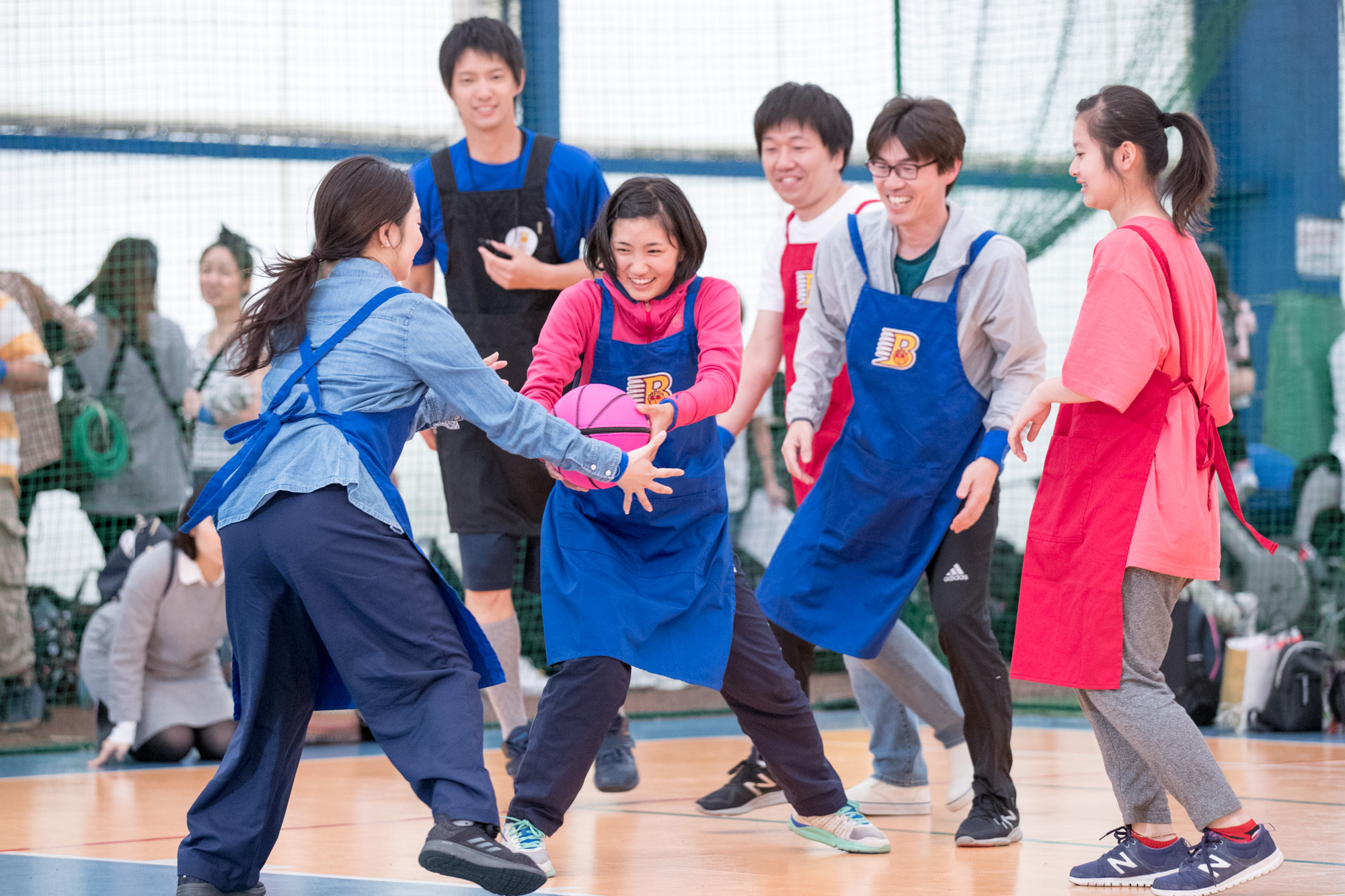 【写真】エプロンをつけたプレーヤーたちがピンク色のバスケットボールを受け渡している様子
