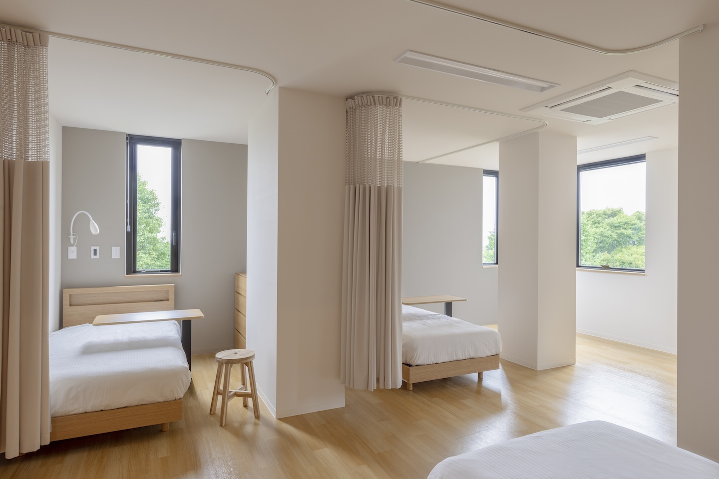 ベッドが並んだ部屋の風景。窓からは外の木の緑色が見える