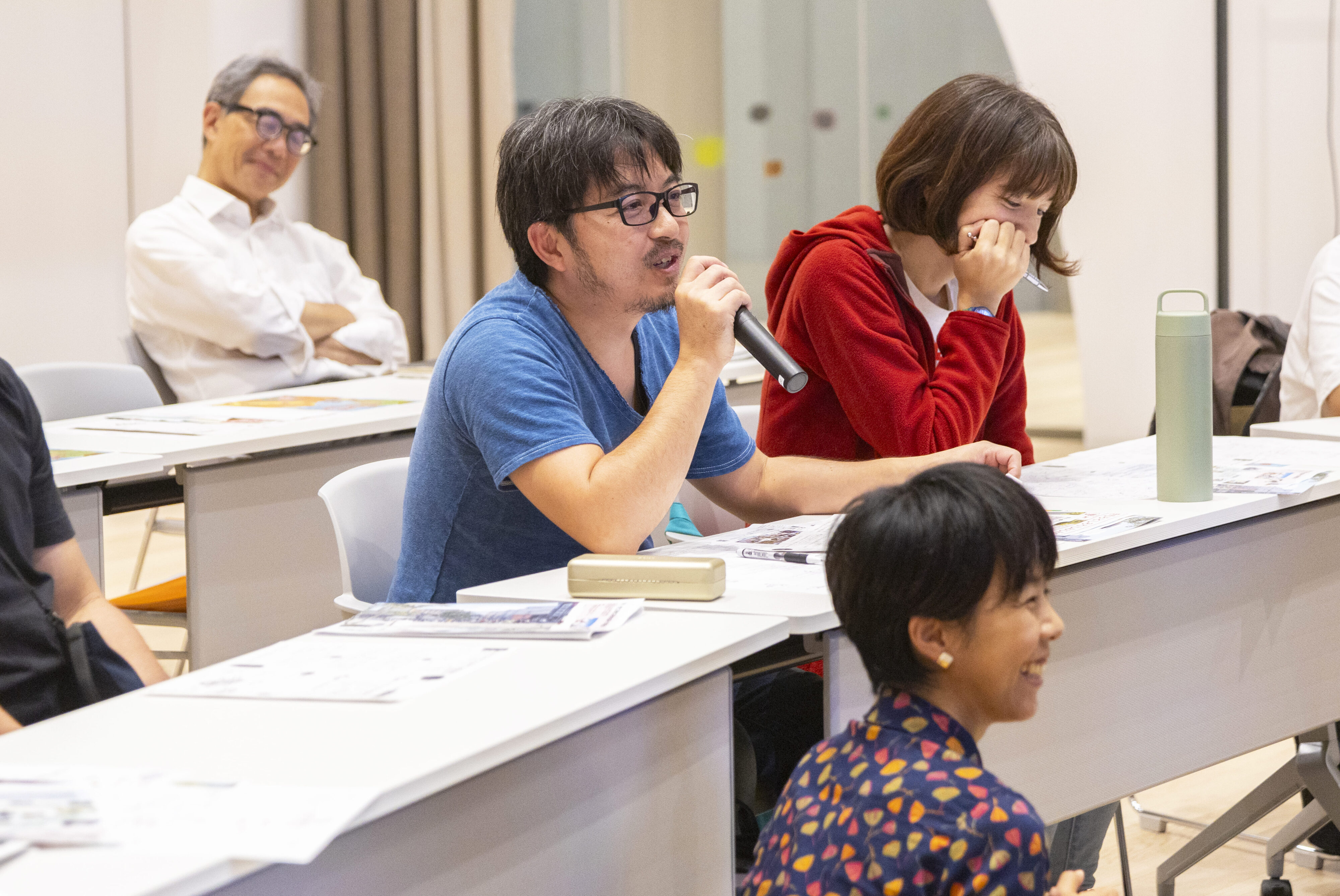 【写真】白い長机について、マイクを手に話す参加者