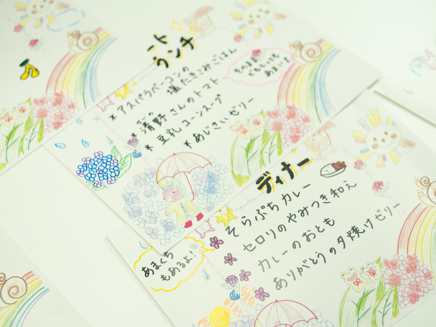 【写真】虹や太陽、紫陽花などの手描きイラストと一緒に、ランチとディナーの献立が書かれたカード