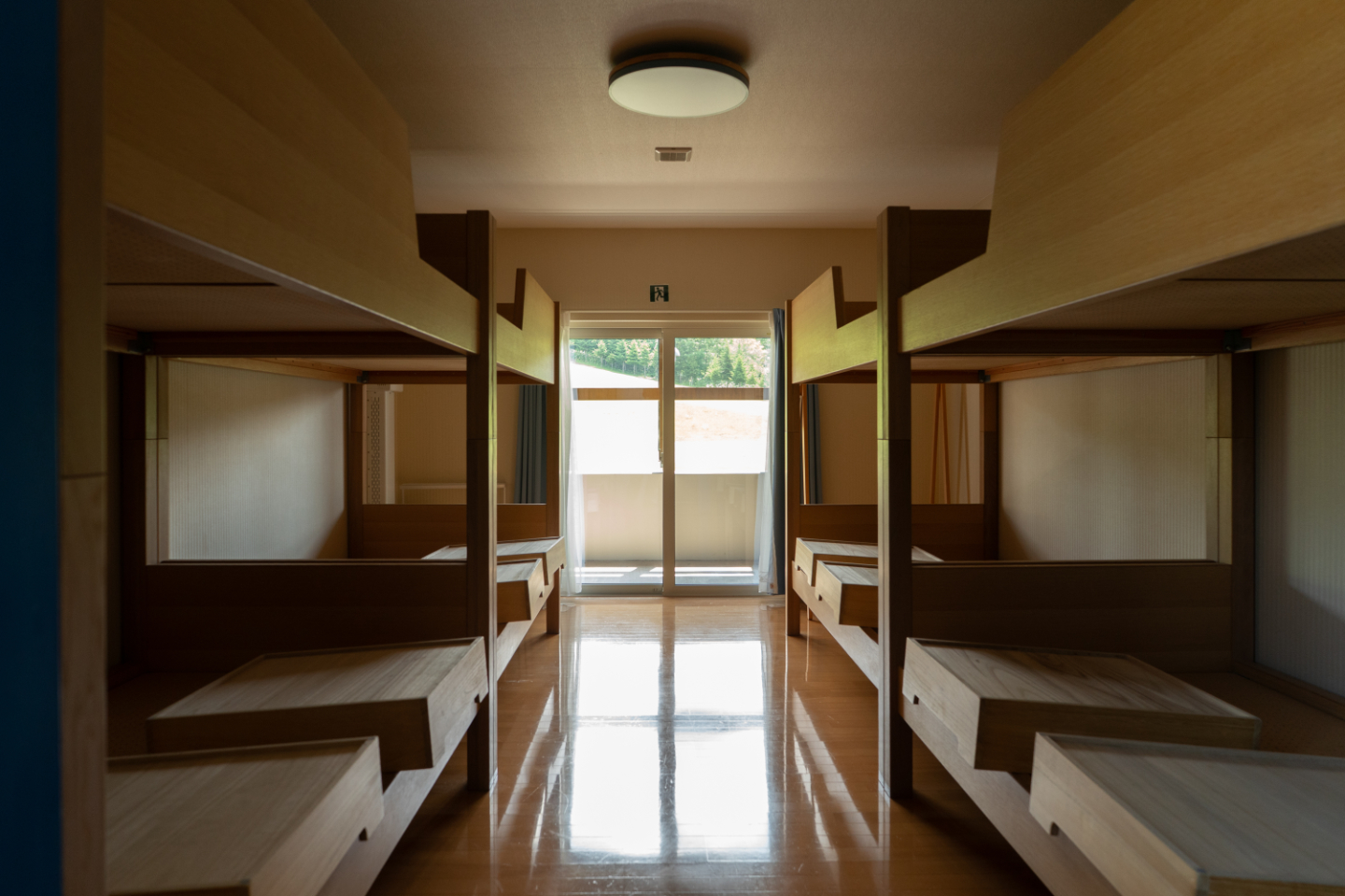 【写真】木製の2段ベッドが左右に並ぶ宿泊部屋。奥には明るい窓があり、自然光が差し込んでいる