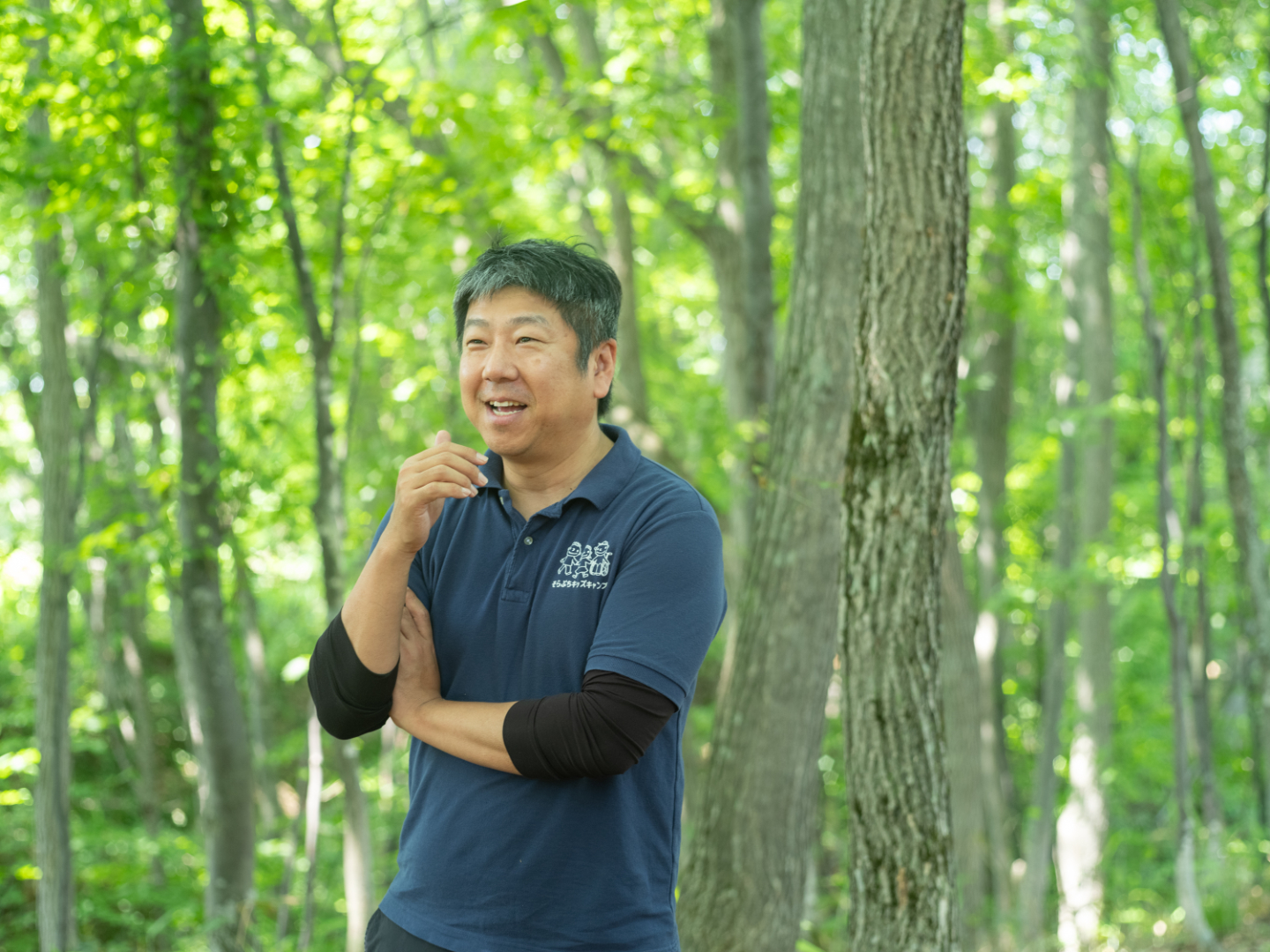 【写真】緑に包まれた森の中で笑顔を見せながら立つ佐々木さん