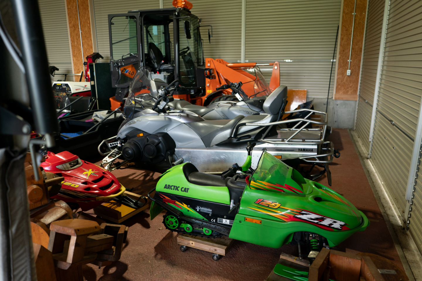 【写真】屋内の倉庫に、YAMAHAのスノーモービル、赤と緑の子供用スノーモービル、オレンジ色の除雪車などの乗り物が整然と並ぶ
