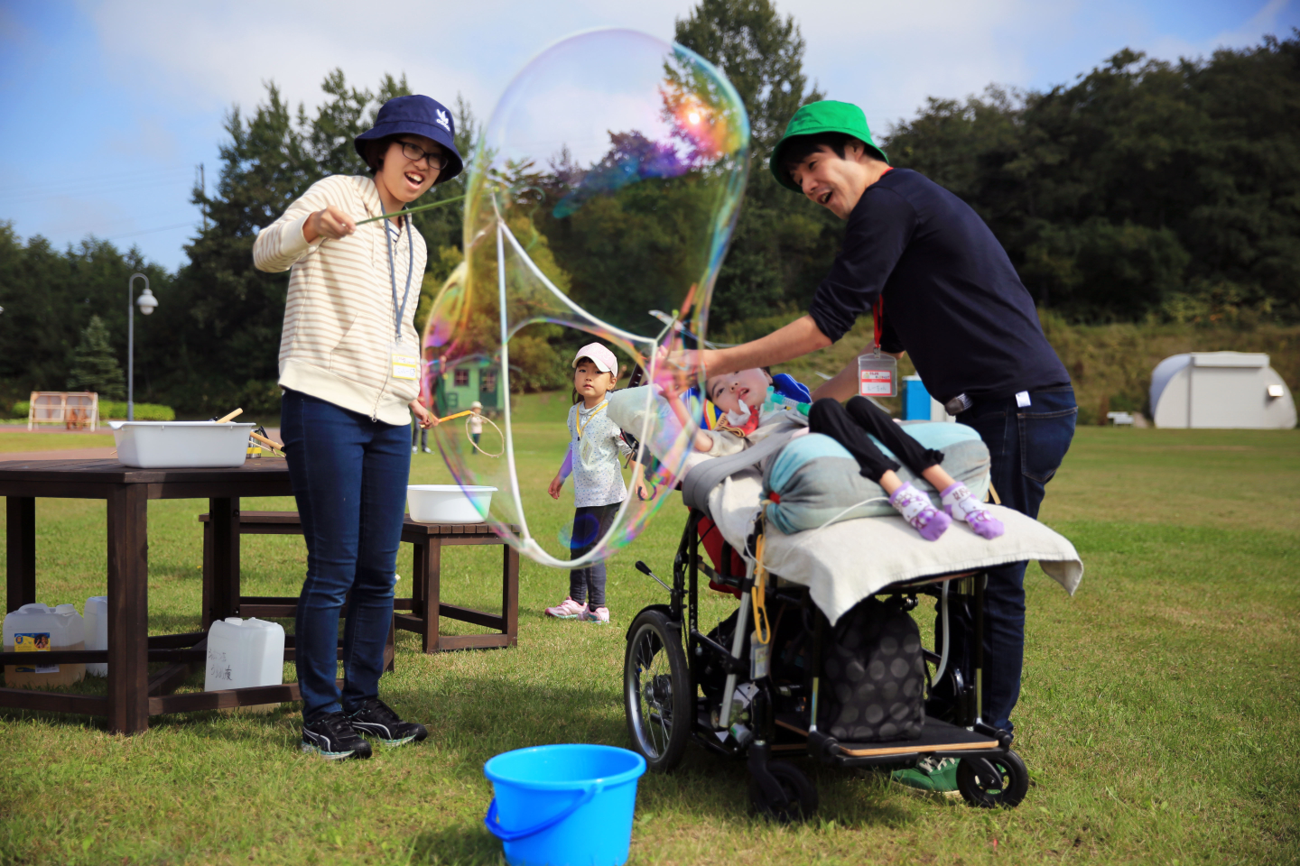 【写真】バギーの上に横になる子どものそばで、大きなシャボン玉をつくっている。