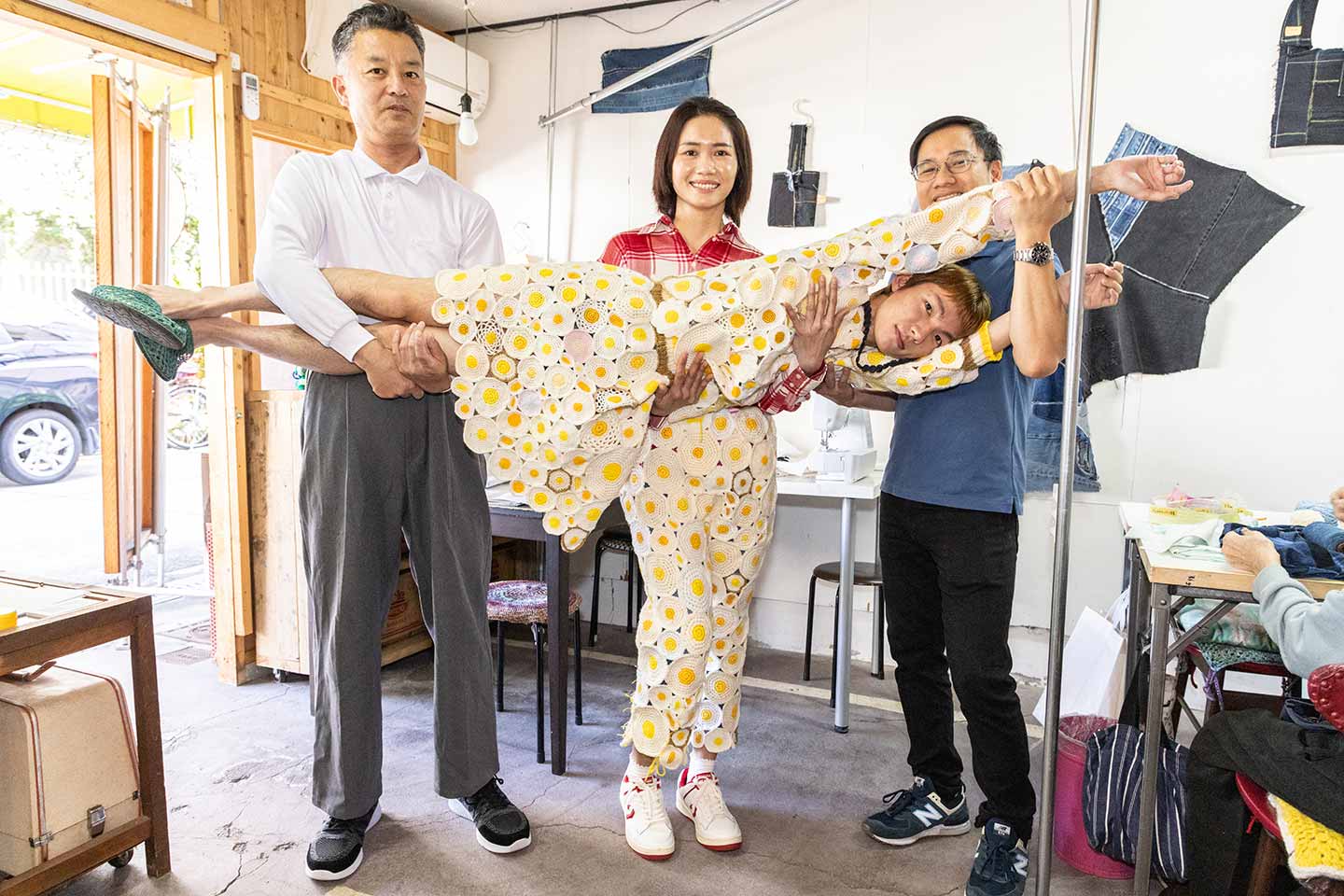 目玉焼きをたくさんパッチワークしたようなデザインの服をまとった男性を抱える3人の男女の写真
