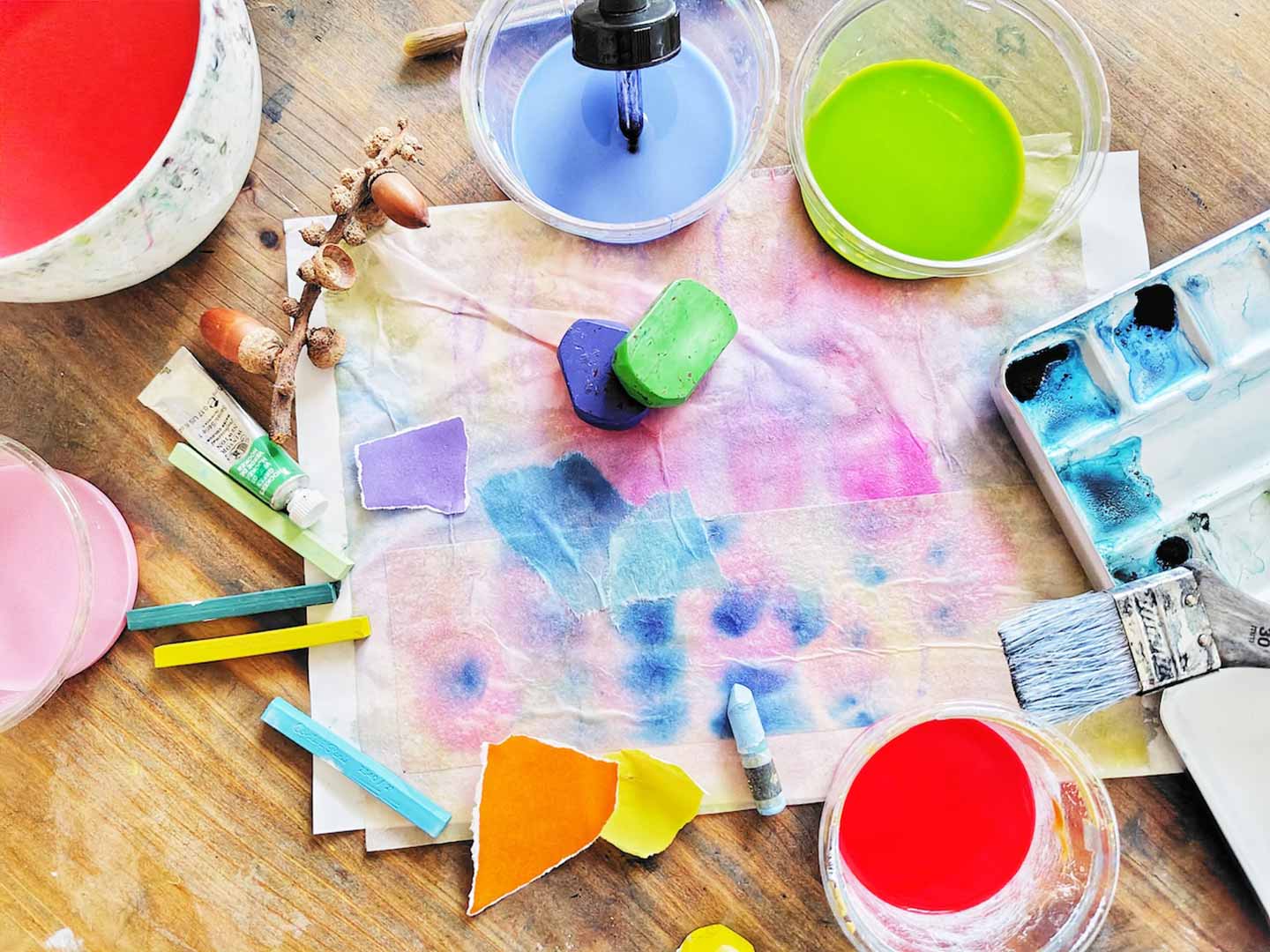 カップに入ったさまざまな水絵具、クレパス、ちぎり絵などと一緒に、滲み絵が中央に置かれた俯瞰写真。