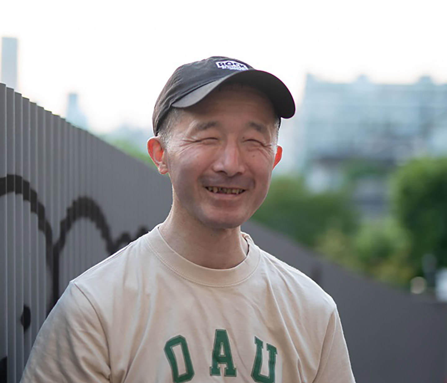 Tシャツとキャップを被ったスタイルで、にこりと微笑む白鳥建二さんの写真。
