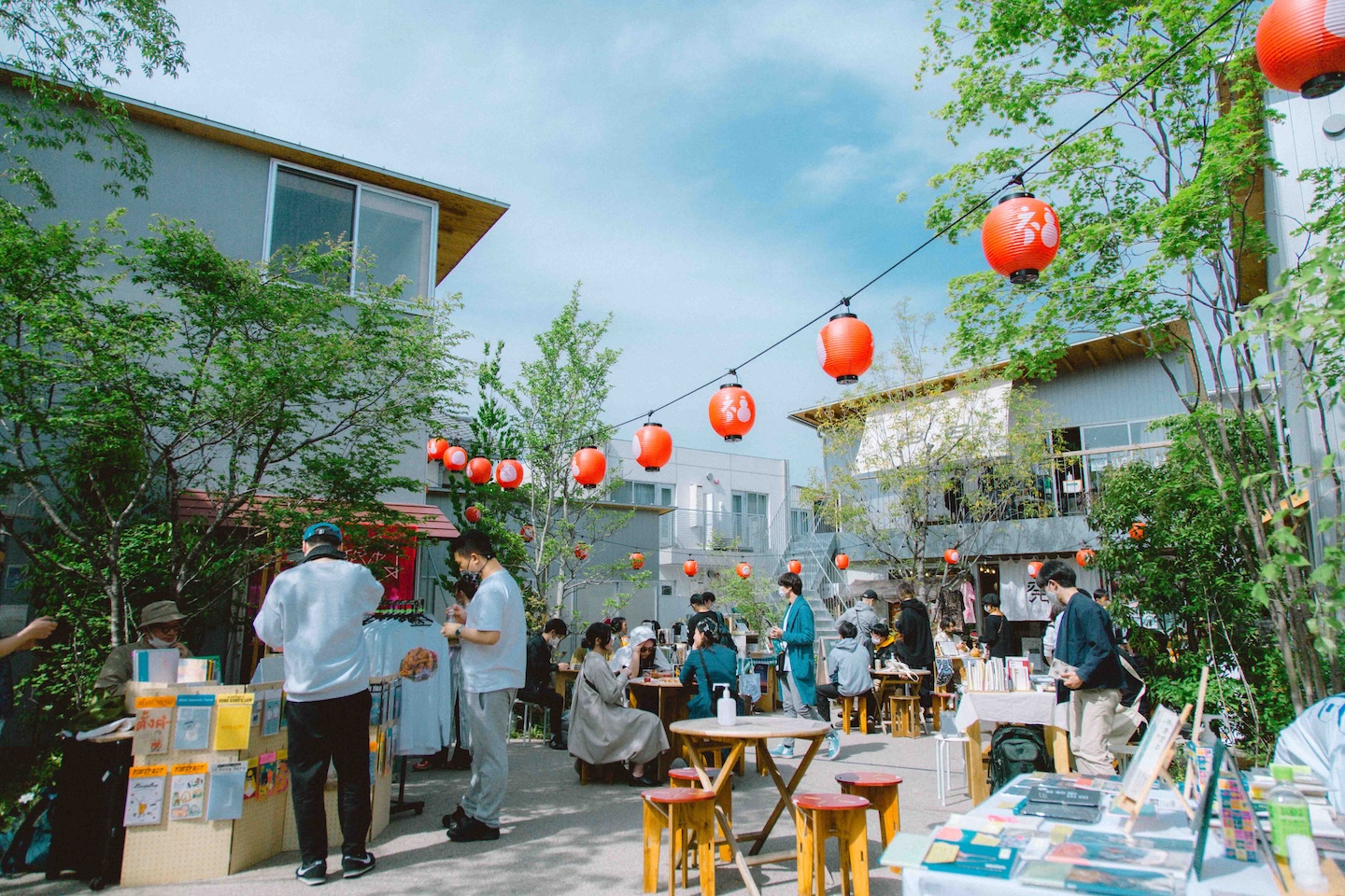 中庭のような場所で、出店する人、買い物する人、テーブルの前の椅子でくつろいでいる人などが集っている