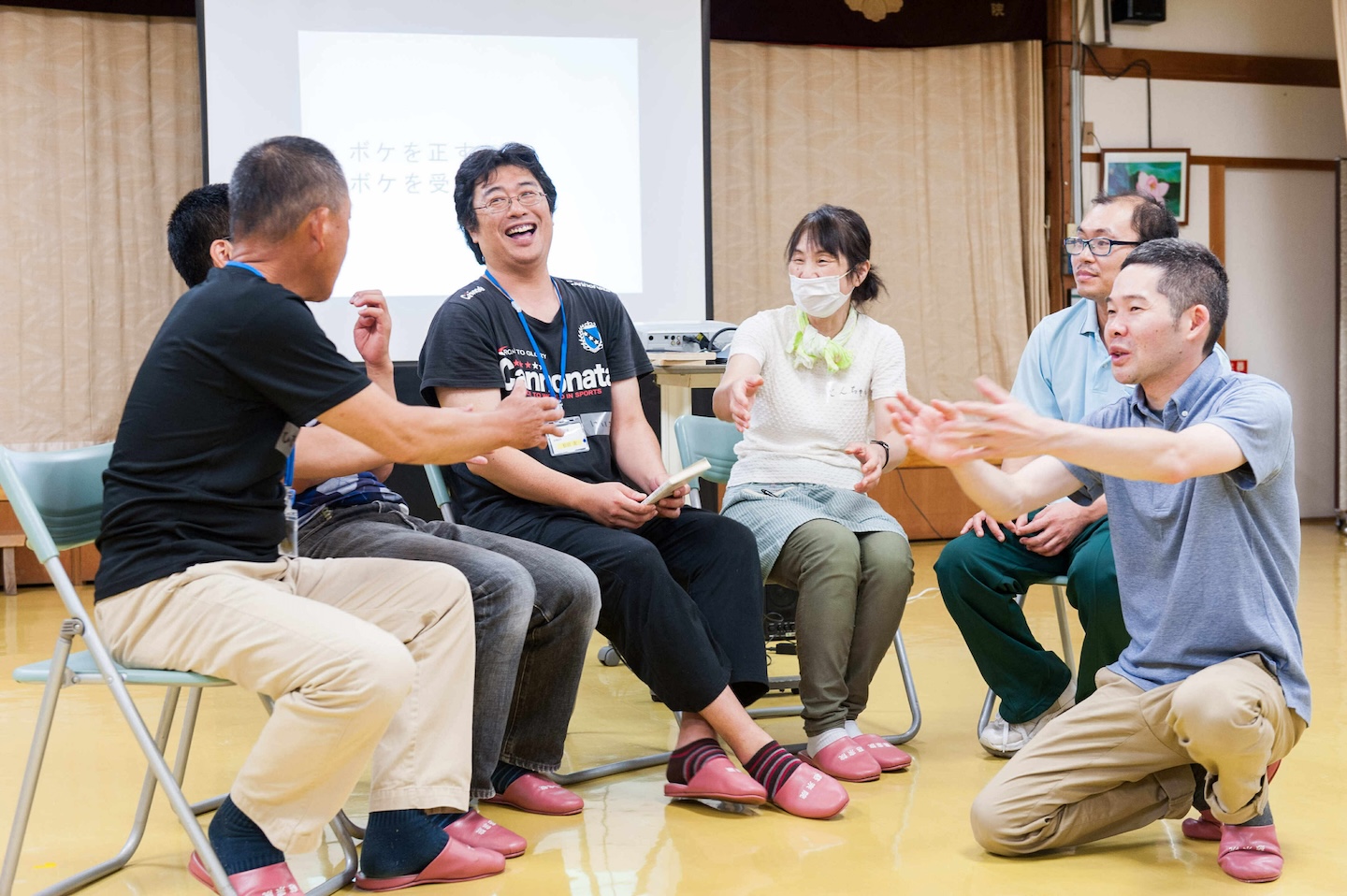 椅子に座ったワークショップ参加者5人が顔を見合わせて笑っている。右端には、菅原さんがしゃがんで両腕を前に出し、なにかアドバイスをしている様子