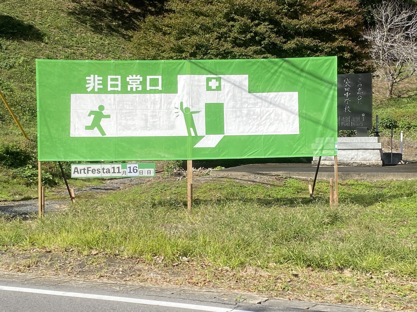 非常口の看板と似た色合いの緑色を背景に、白色の病院の絵、ドアを示している人、駆け込む人が描かれている