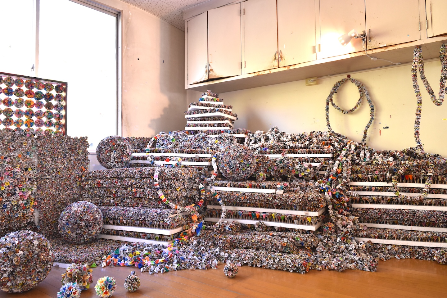 色とりどりの折った紙で作られた小さな造形物が固まって、球体になったり、紐のようになったり、積み重なったりしている