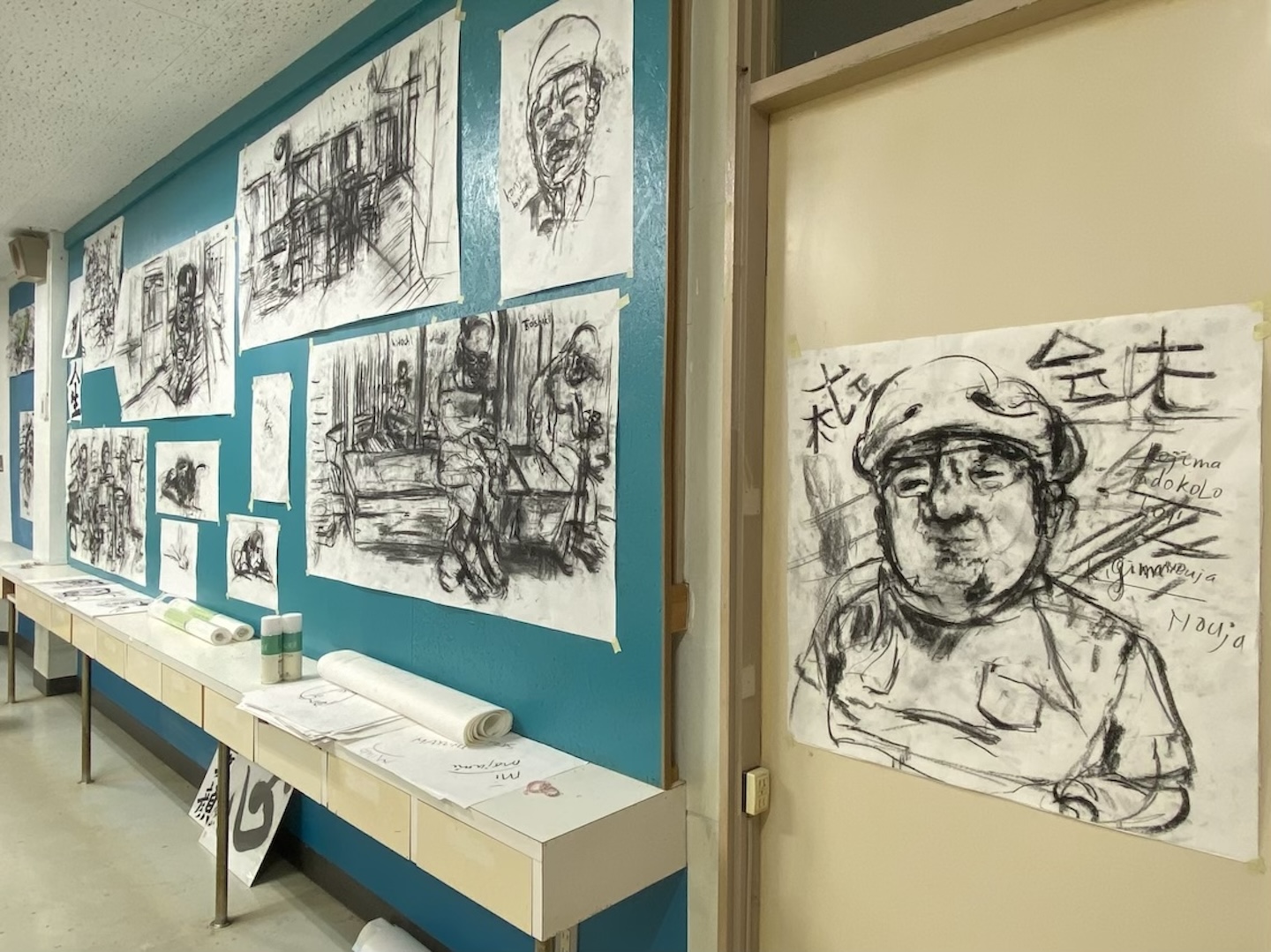 青緑色の壁に、顔や椅子に腰掛ける人の姿が黒い線で描かれている