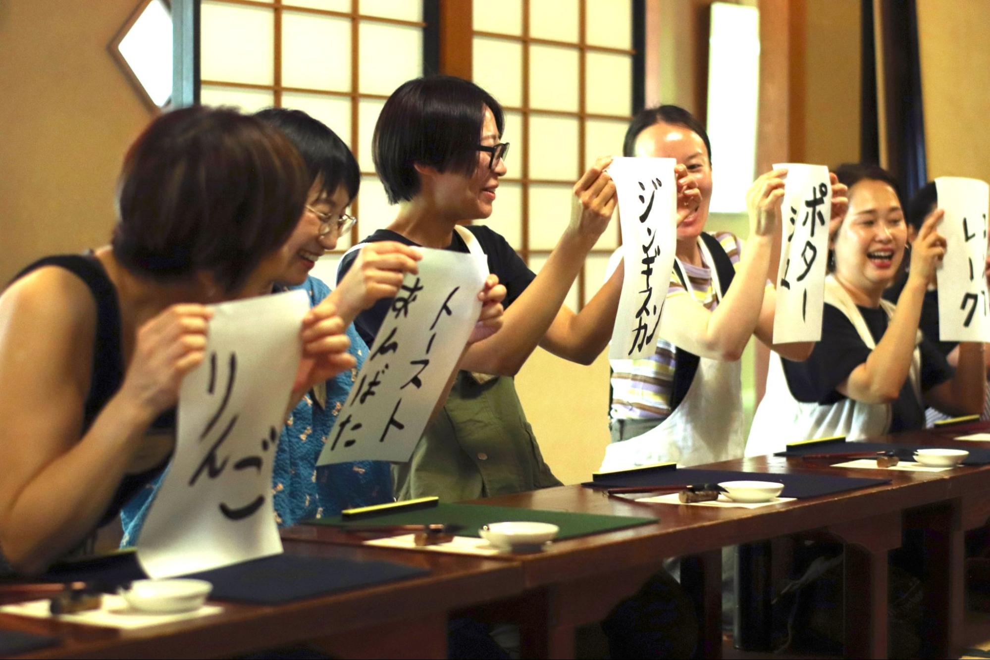 【写真】りんご、トマトなど、半紙に炭で書いた文字を掲げる人々