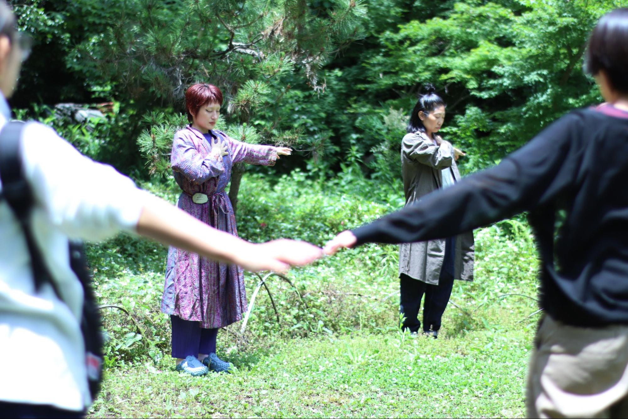 【写真】一面の緑の中に手を広げ佇む人びと