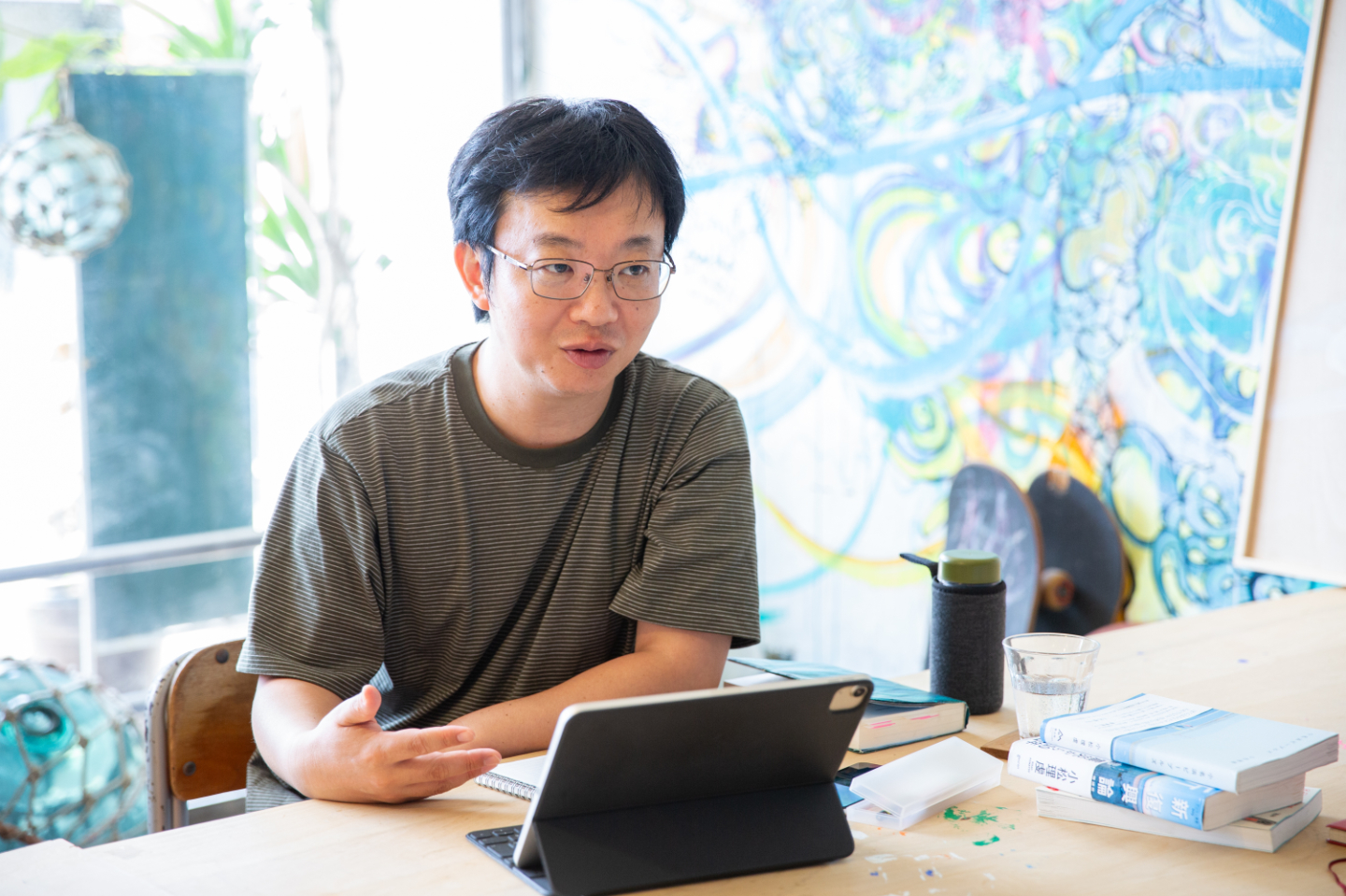 【写真】テーブルについた青山さん。机の上にはタブレットが広げられている