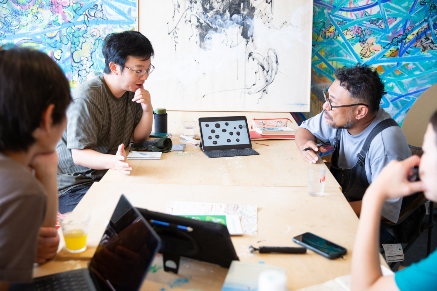 【写真】話し込む青山さんと小松さん。手前にパソコンを広げ聞きいる別の2人の姿
