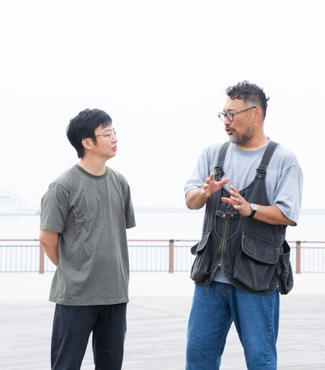 【写真】海をバックに、朝靄の中を向かい合って語りあう青山さんと小松さん