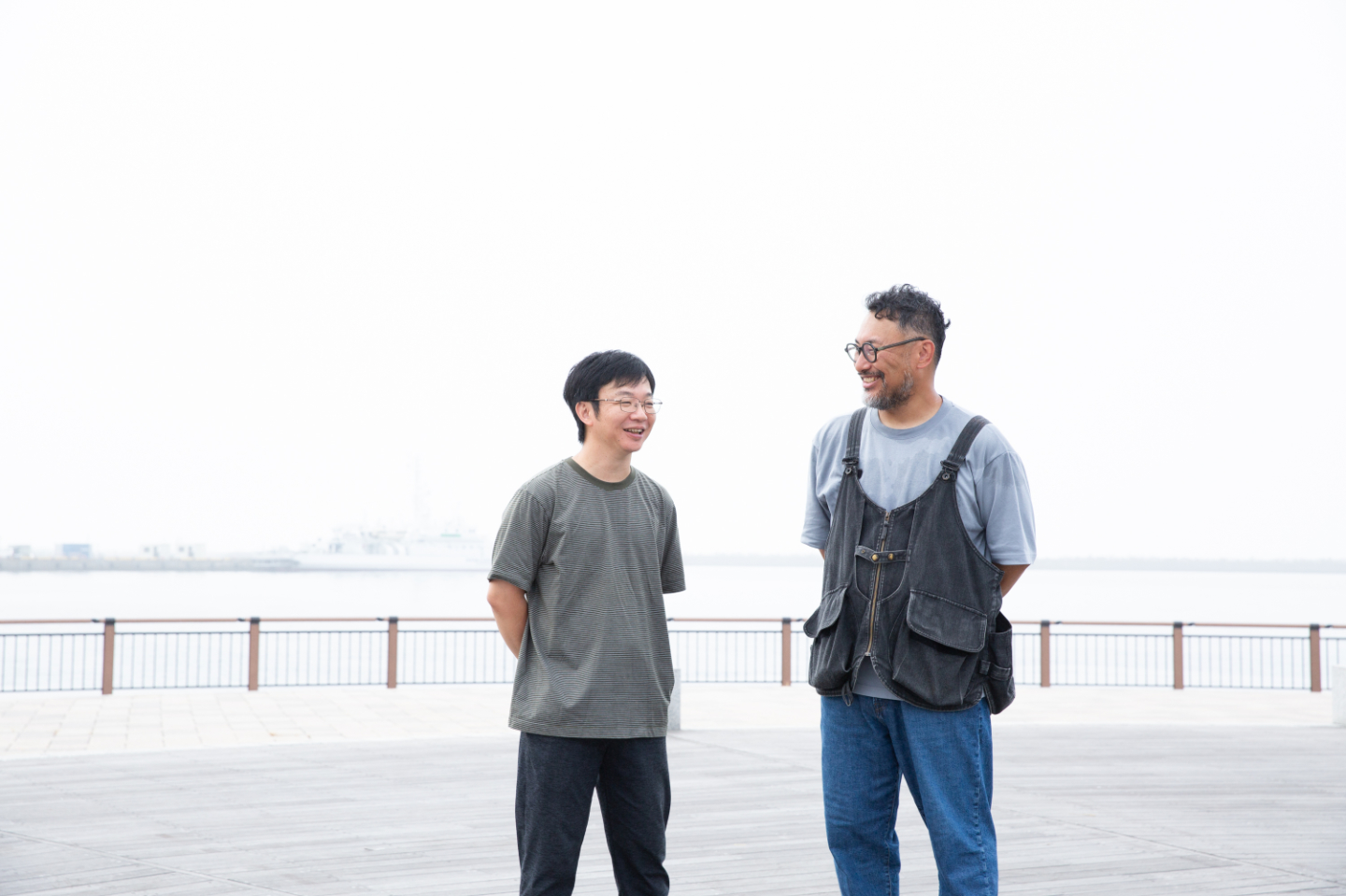 【写真】海辺に佇み、笑顔で話す2人。背景にはもやがかかっている