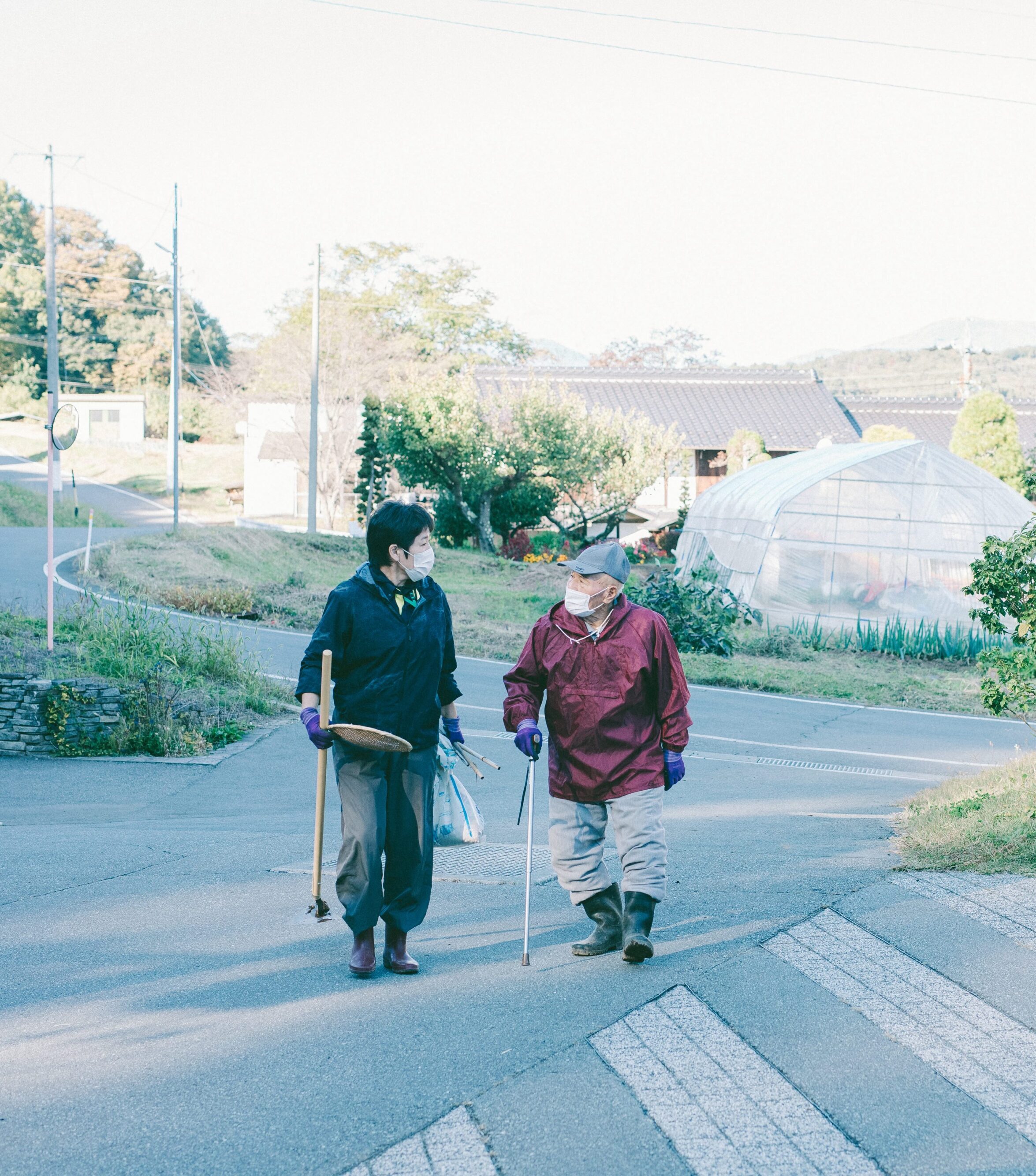 【写真】畑を整備する道具を持って歩く人がふたり、おしゃべりしている。