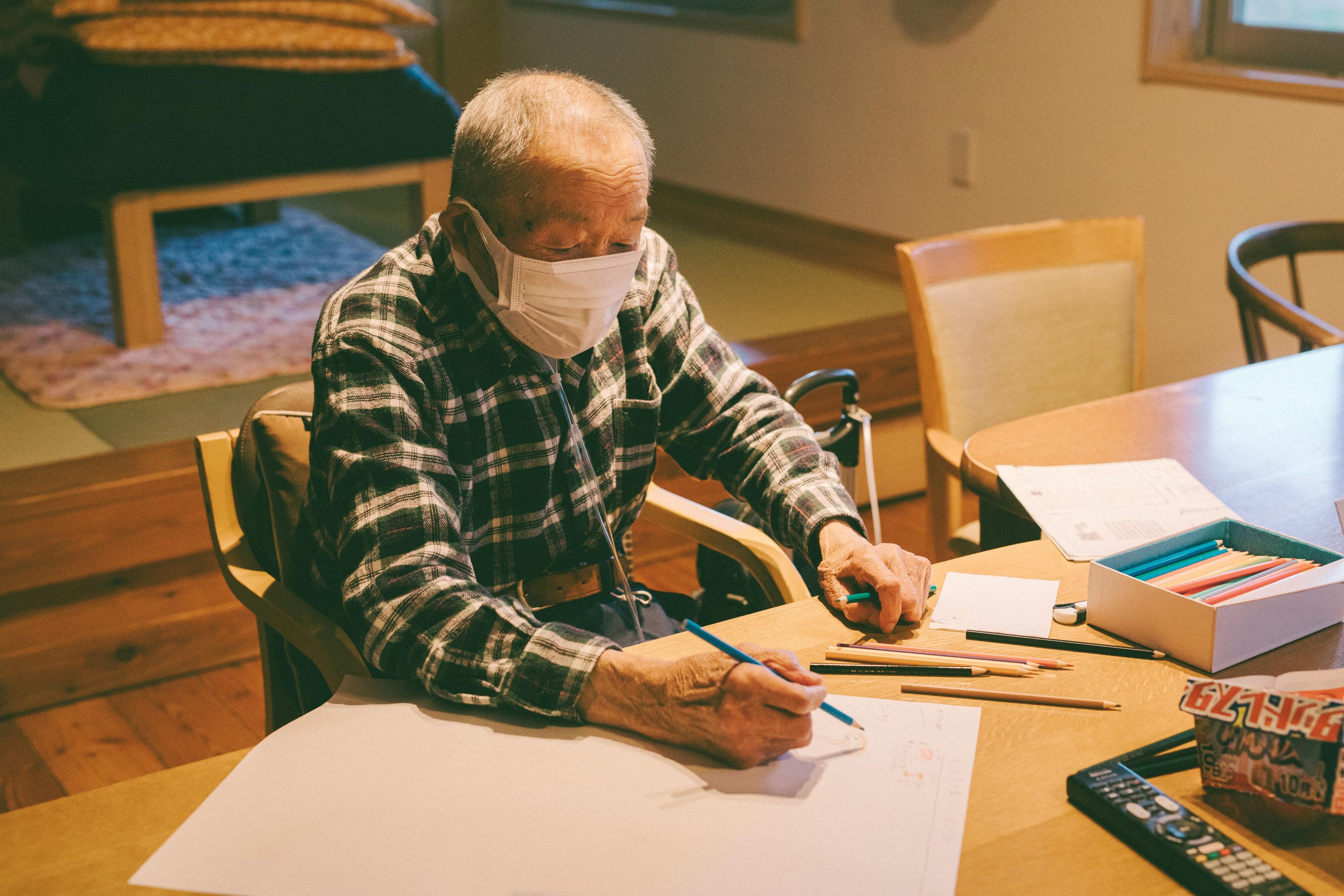 【写真】色鉛筆をもち、イラストを描いているおじいさん