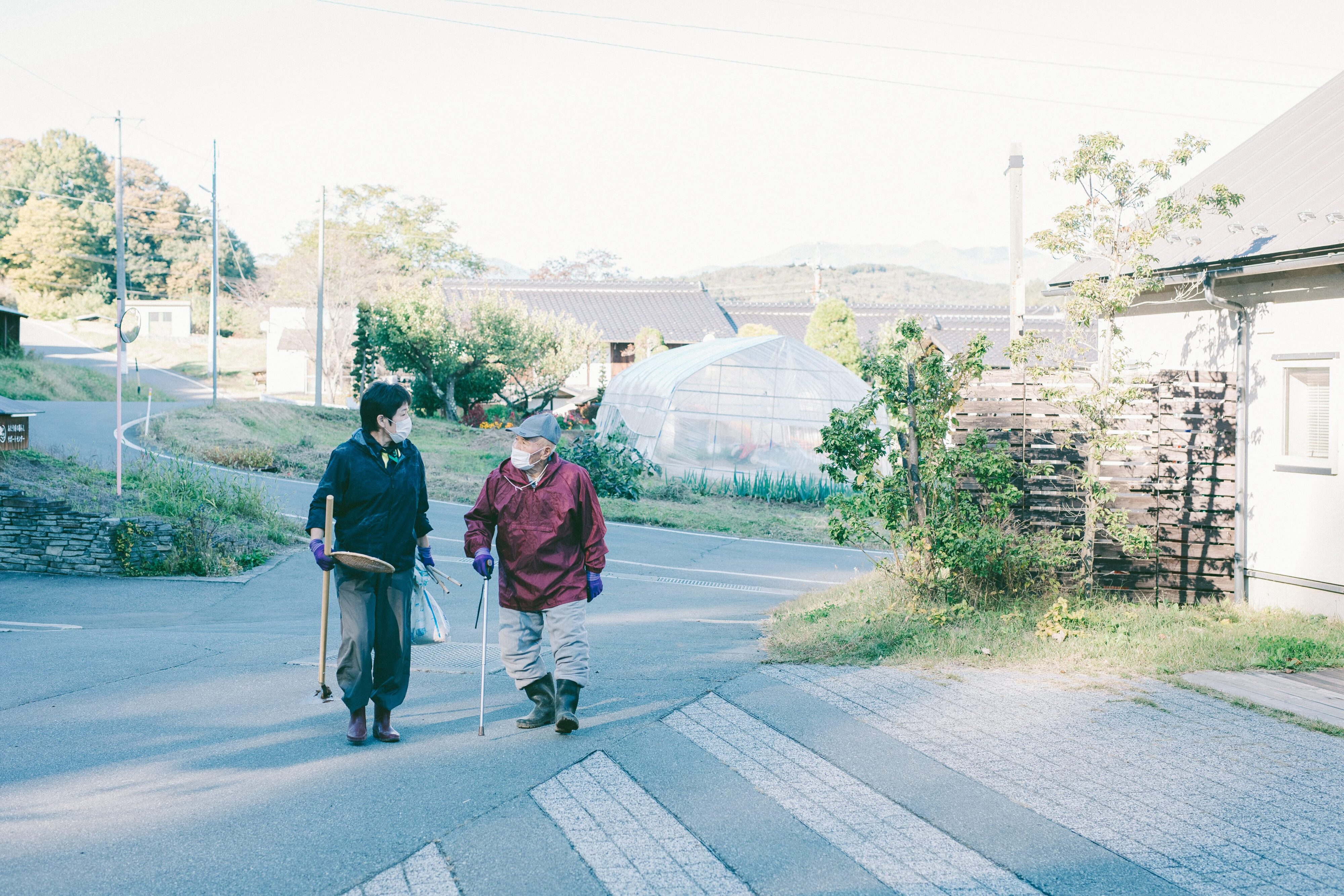 【写真】畑を整備する道具を持って歩く人がふたり、おしゃべりしている。