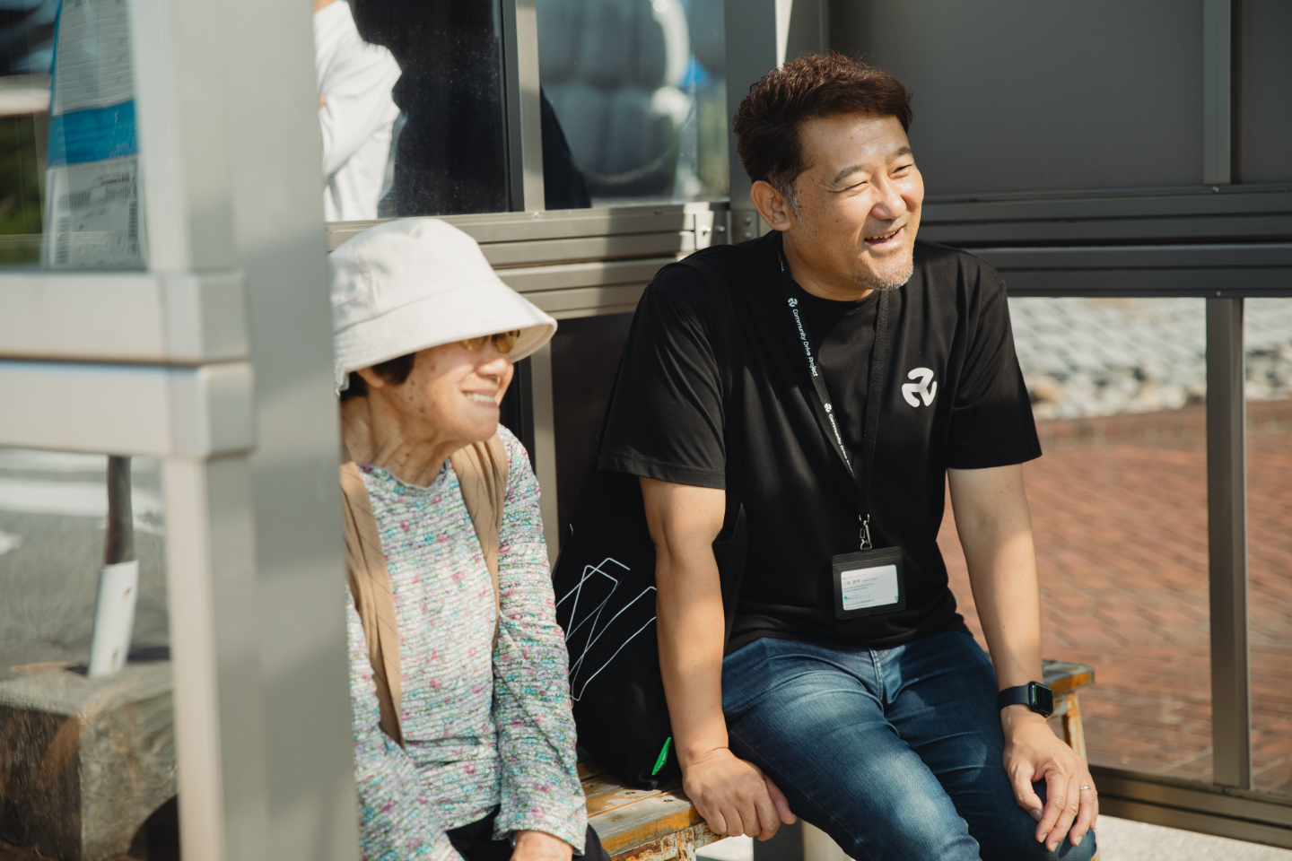 【写真】バス停のベンチに座り笑顔で会話する二人