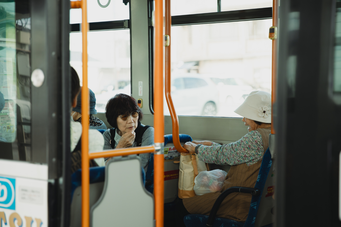 【写真】路線バスの車内で高齢の女性2人が向かい合って話し込んでいる