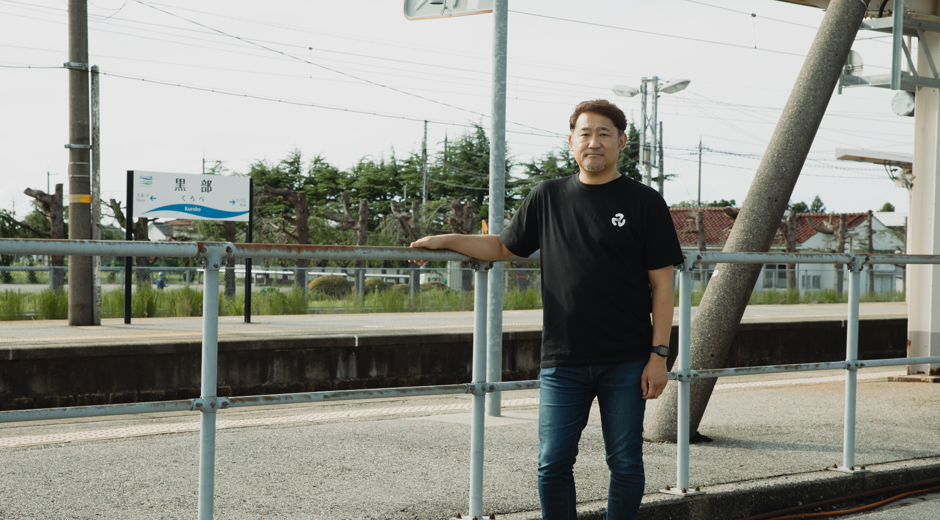 【写真】黒部駅の外に、黒いTシャツをきたひとりが佇む。手すりに手をかけている