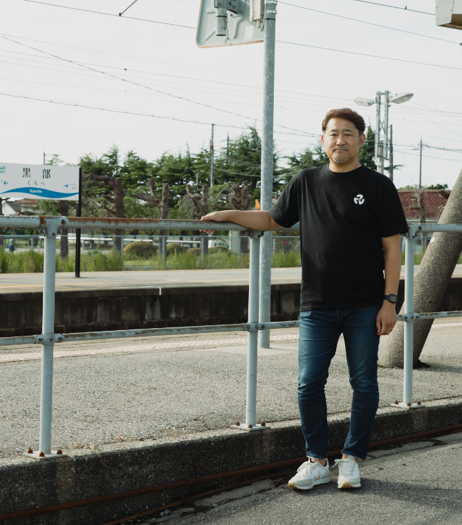 【写真】黒部駅の外に、黒いTシャツをきたひとりが佇む。手すりに手をかけている