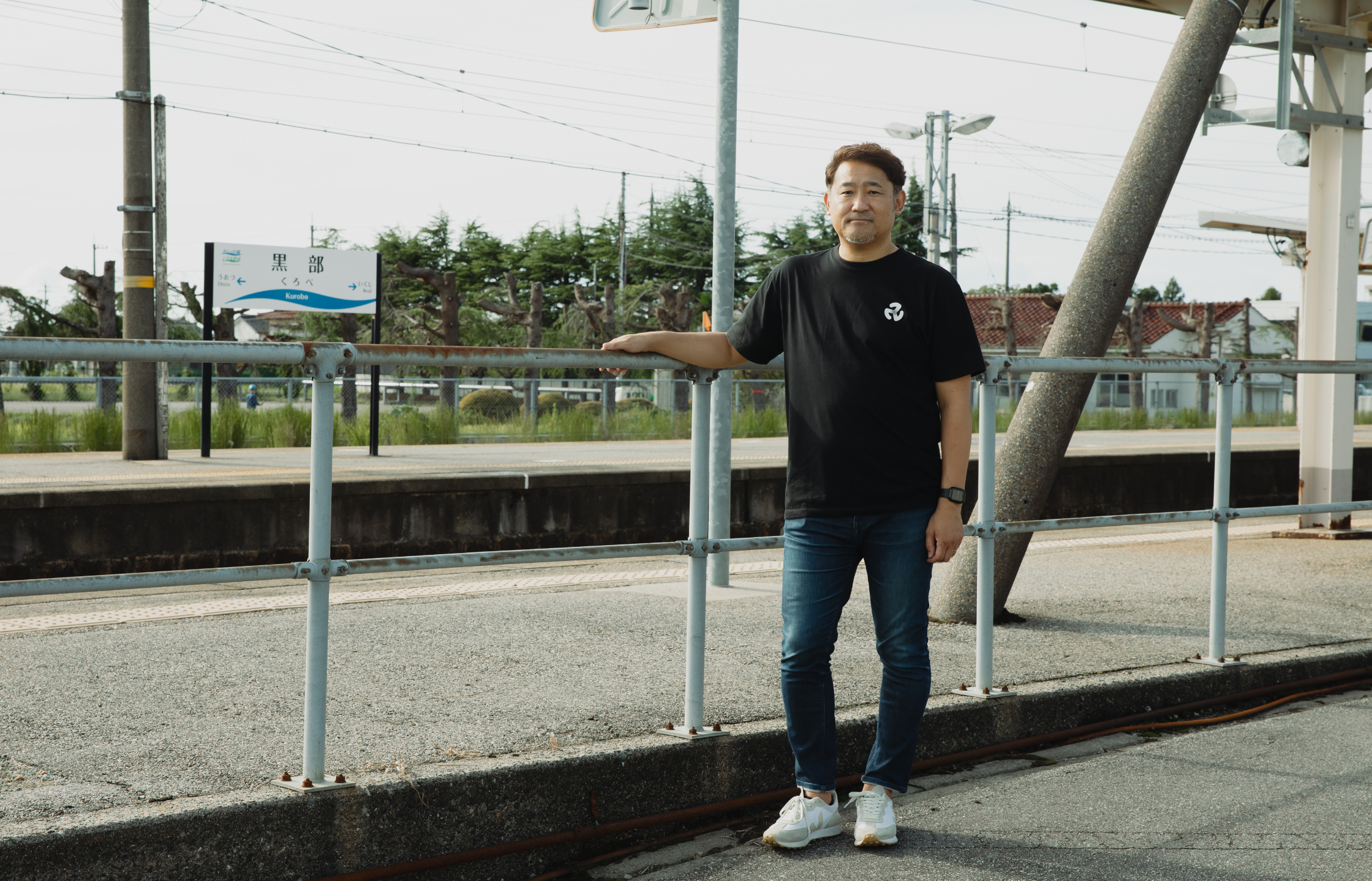 【写真】黒部駅の外に、黒いTシャツをきたひとりが佇む。手すりに手をかけている