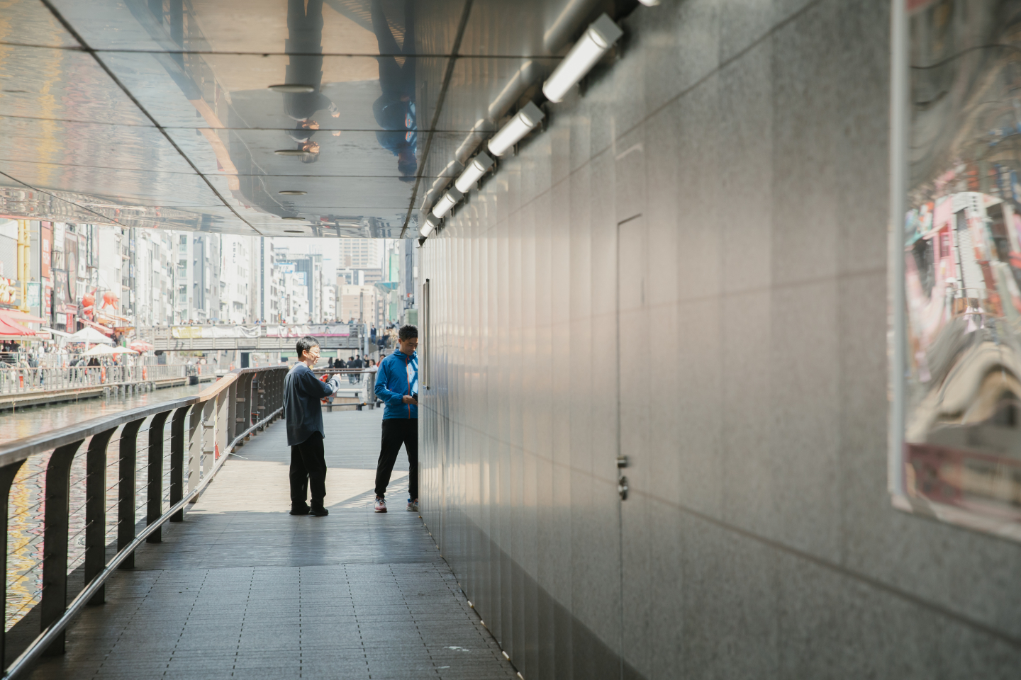 【写真】ガード下で話し込む2人。背景には運河とにぎやかな街並みが見える