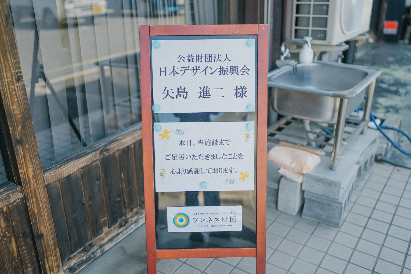 【写真】屋外に設置された立て看板に、日本デザイン振興会矢島様と書かれた紙が貼られている