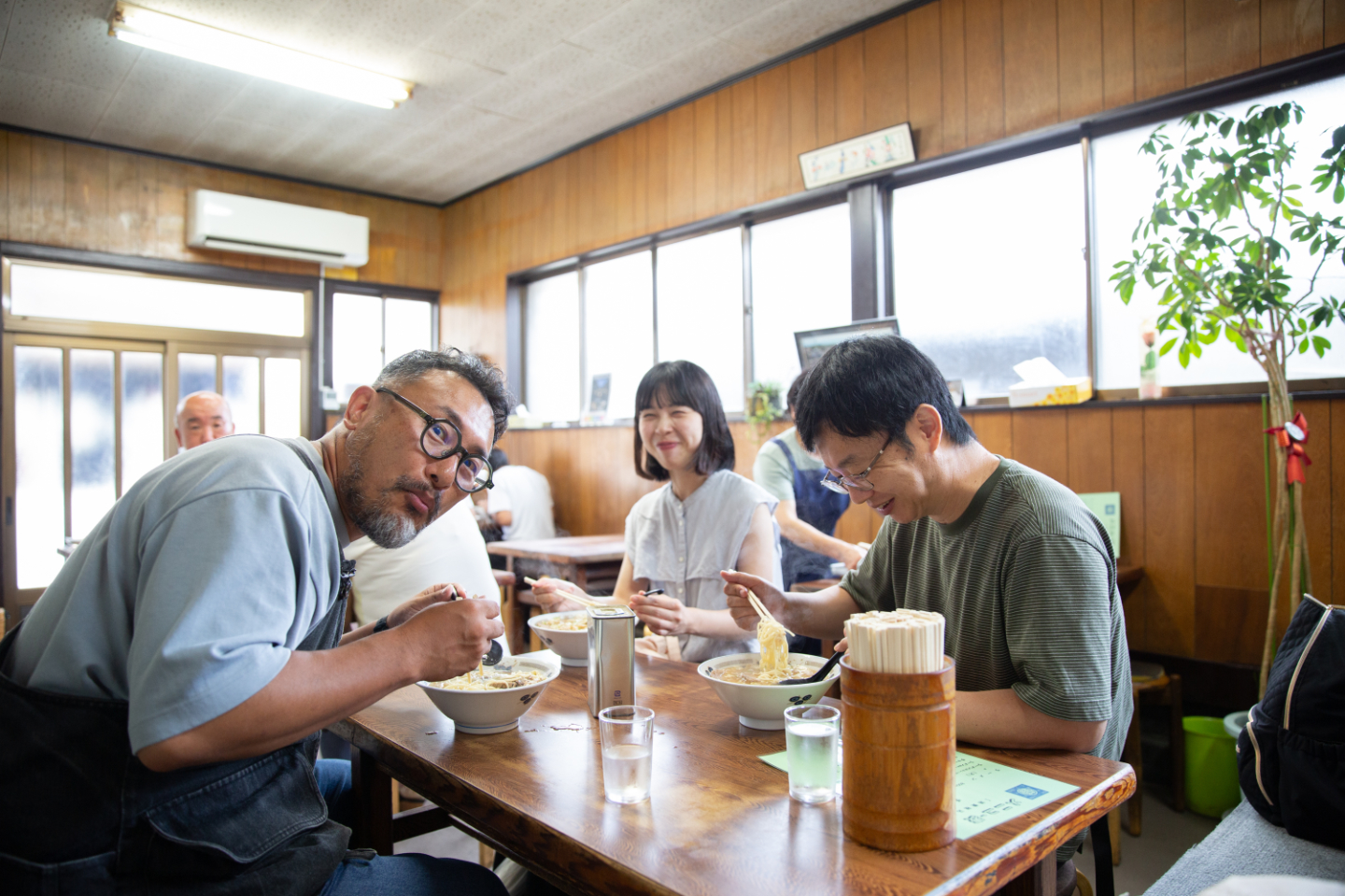 【写真】木のテーブルを囲んで3人がラーメンを食べている