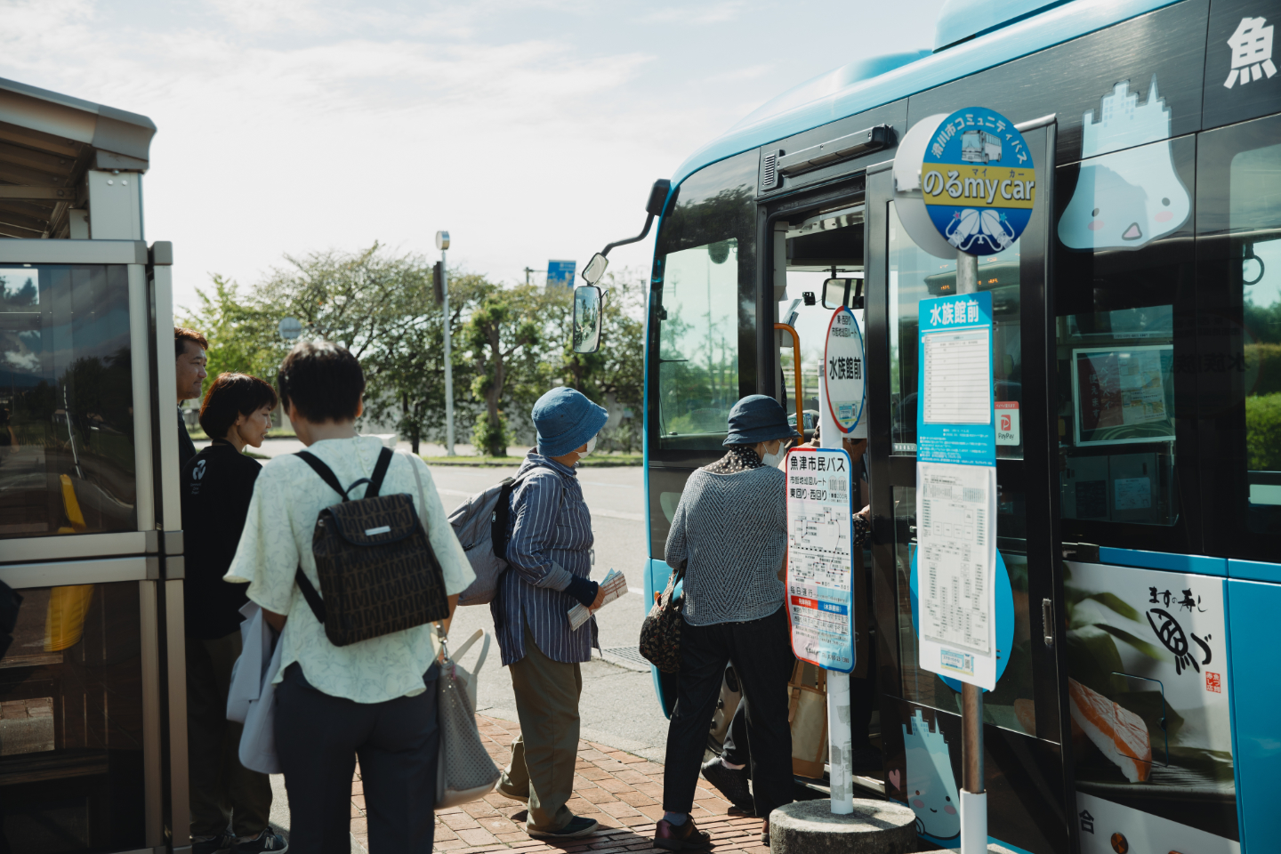 【写真】青色の小さなバスに乗り込む高齢者の方々。コミュニティバスの表示の下には、のるマイカーの文字