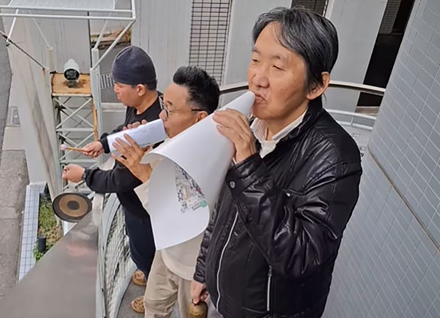 男性３名が太鼓を叩いたりメガホンらしきもので誰かに呼びかけている写真。