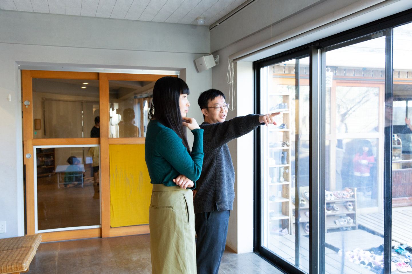 【写真】大きなガラス扉の前で、2人が外を見ながら話をしている様子。青山さんが外を指さし、寺尾さんが隣で真剣に耳を傾けている