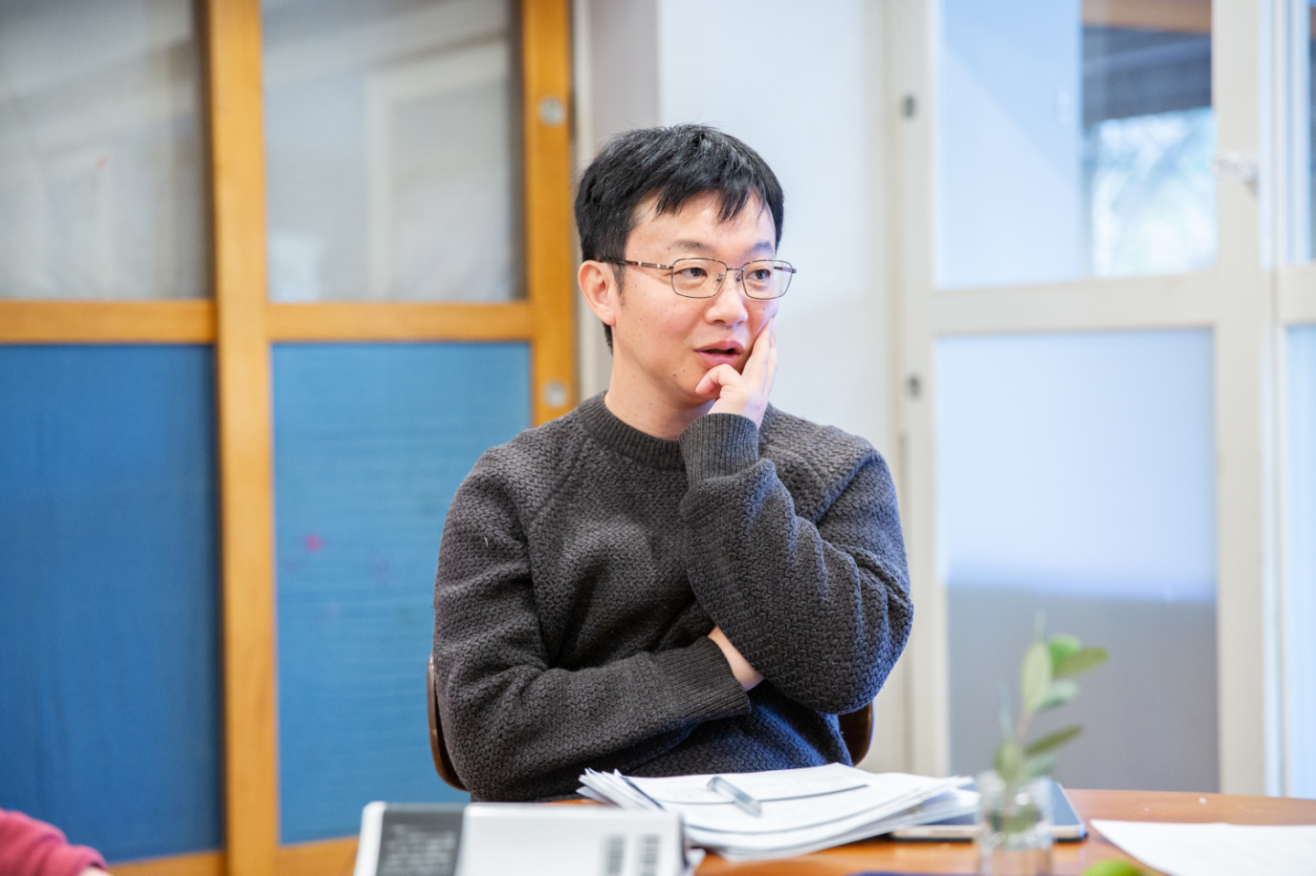 【写真】書類が置かれたテーブルで、が頬に手を当てながら話を聞く青山さん