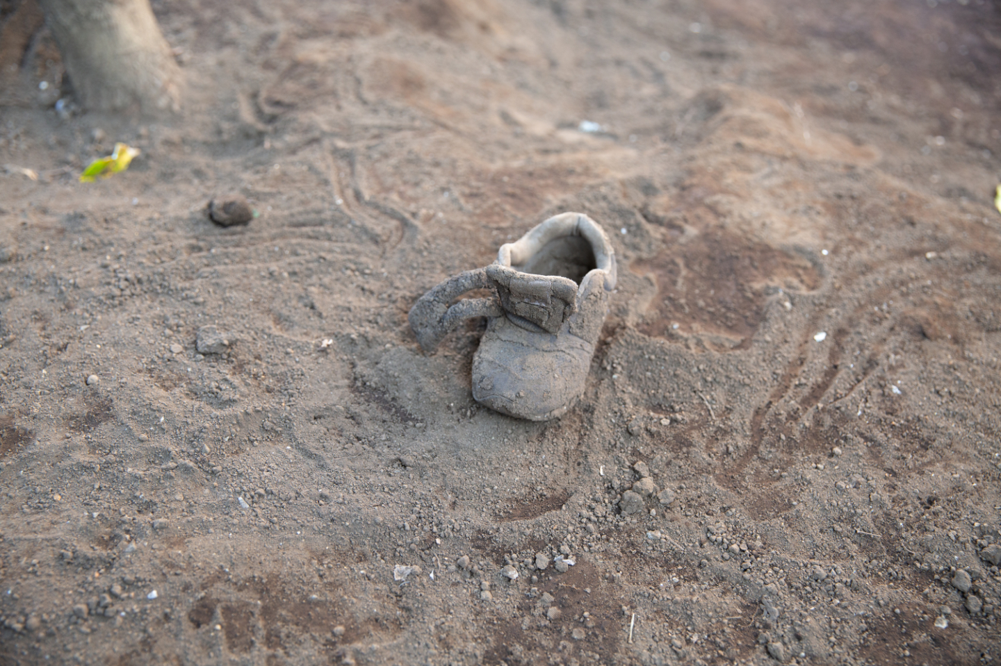 【写真】土の地面にぽつんと置かれたままの小さな靴。泥まみれで色が同化している
