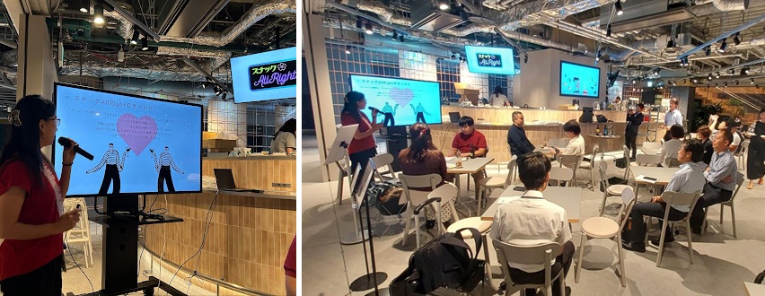 【写真】バーカウンターの前に椅子とテーブルがならび、モニターに写されたプレゼンテーターの資料を参加者が眺めている