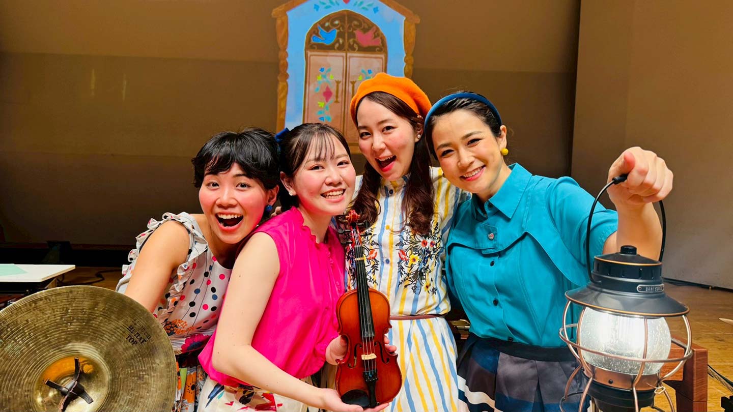 シンバルやバイオリンなどを持った女性4人の写真。