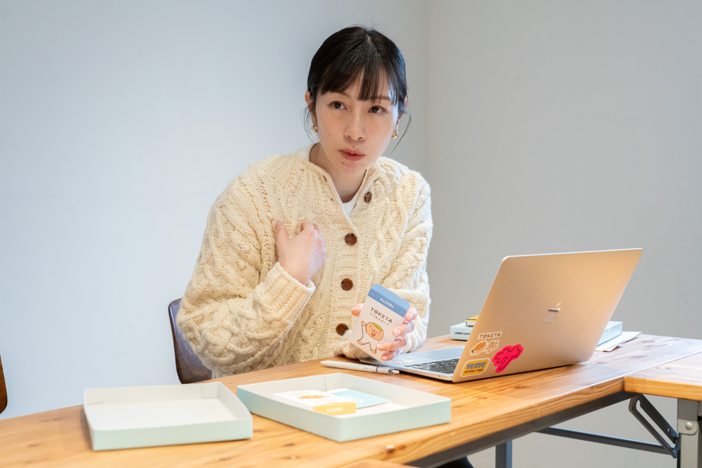 【写真】ノートパソコンの前でカードを手に持ちながら話している新開さん