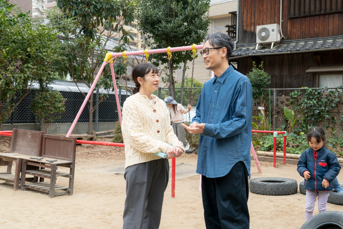 【写真】公園で立ち話をする新開さんと田北さん。背後には遊びまわる子どもたちの姿