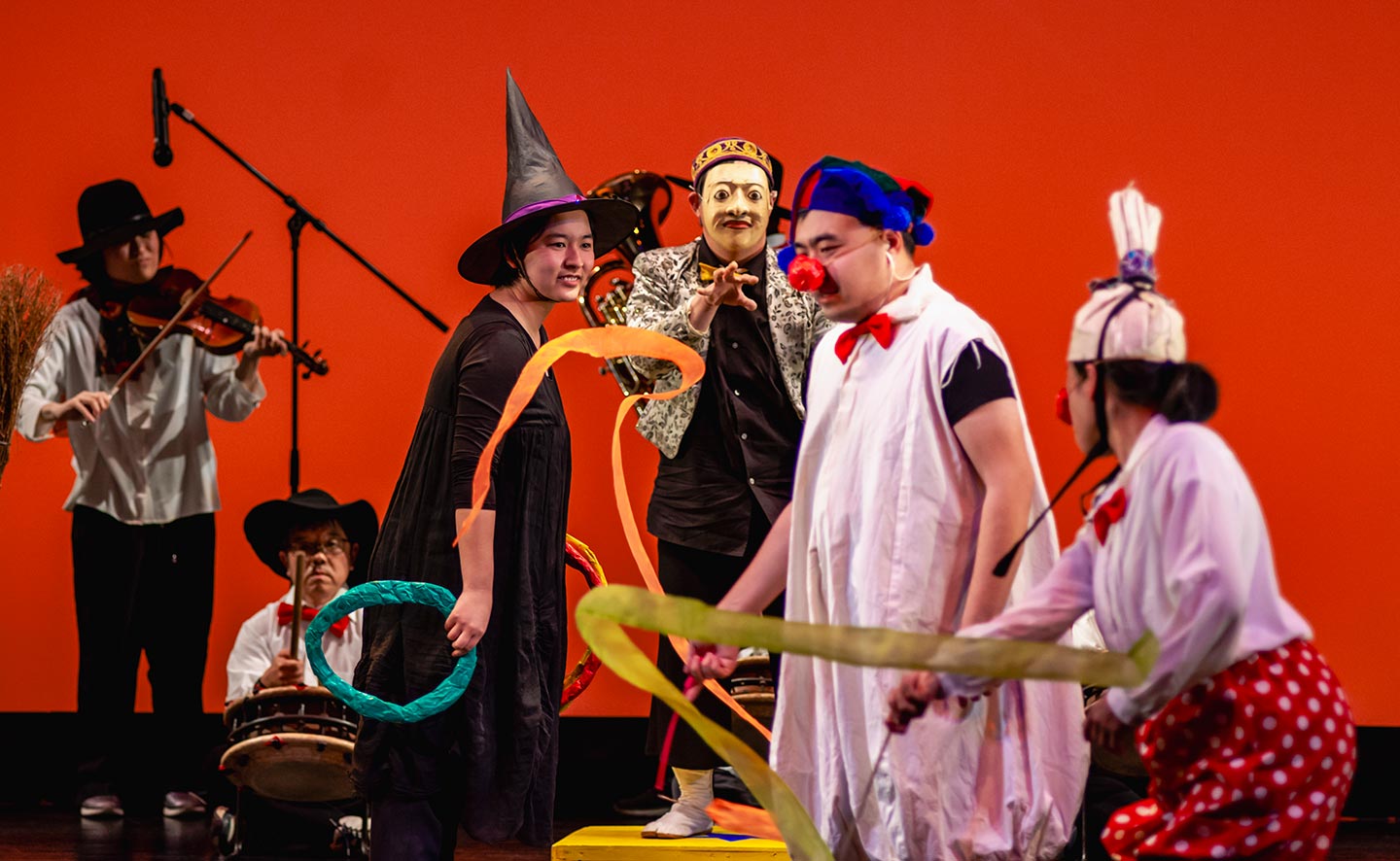 サーカス団のような衣装を着てパフォーマンスや楽器を奏でる人々の写真。